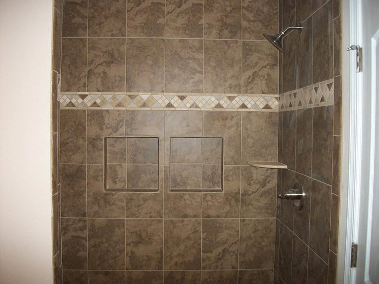 Shower with marble tile walls, chrome shower head, and white door with metal handle
