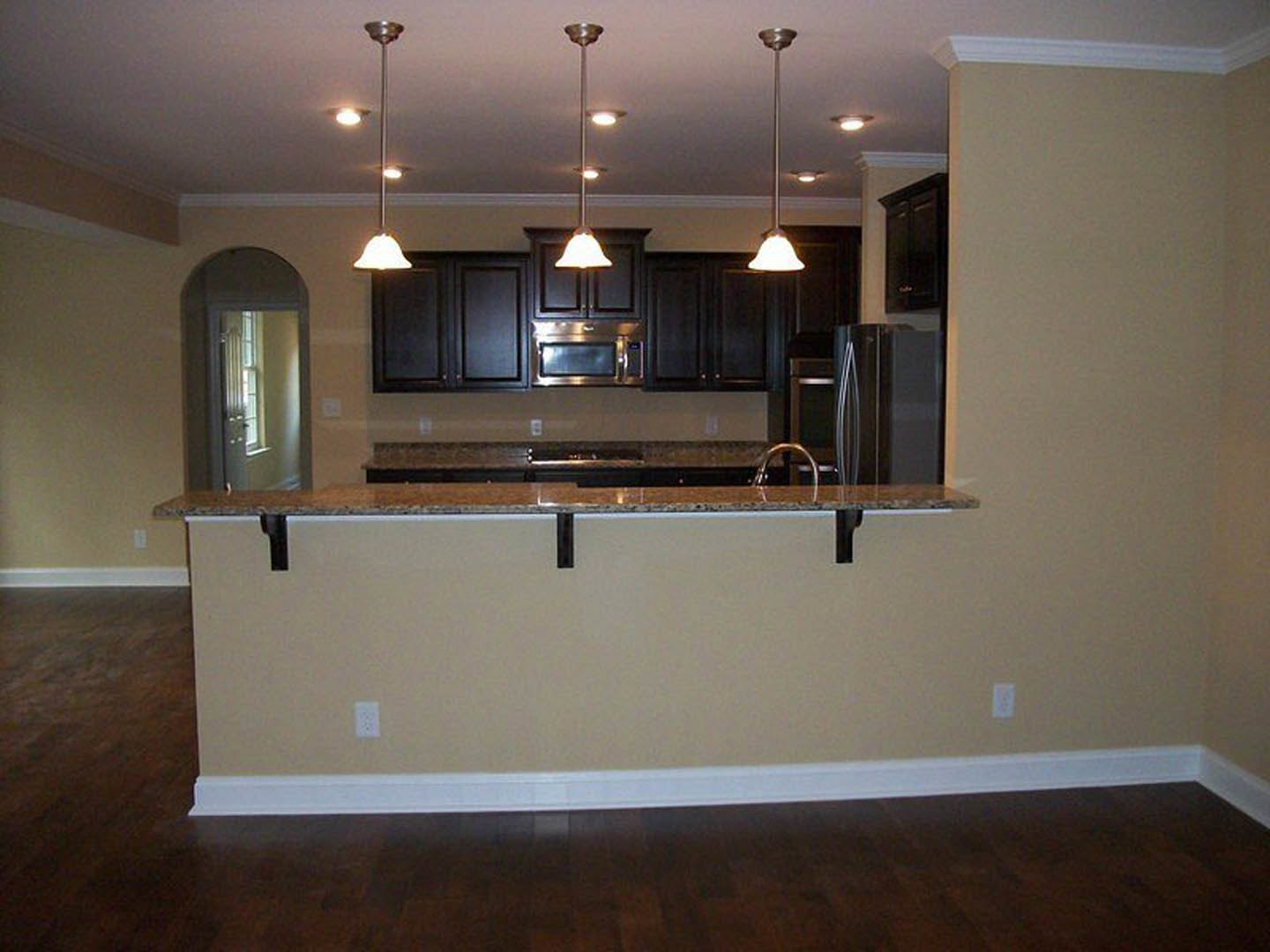 Modern kitchen with white cabinetry, stainless steel refrigerator, stone countertop bar, pendant ceiling light, and wood flooring