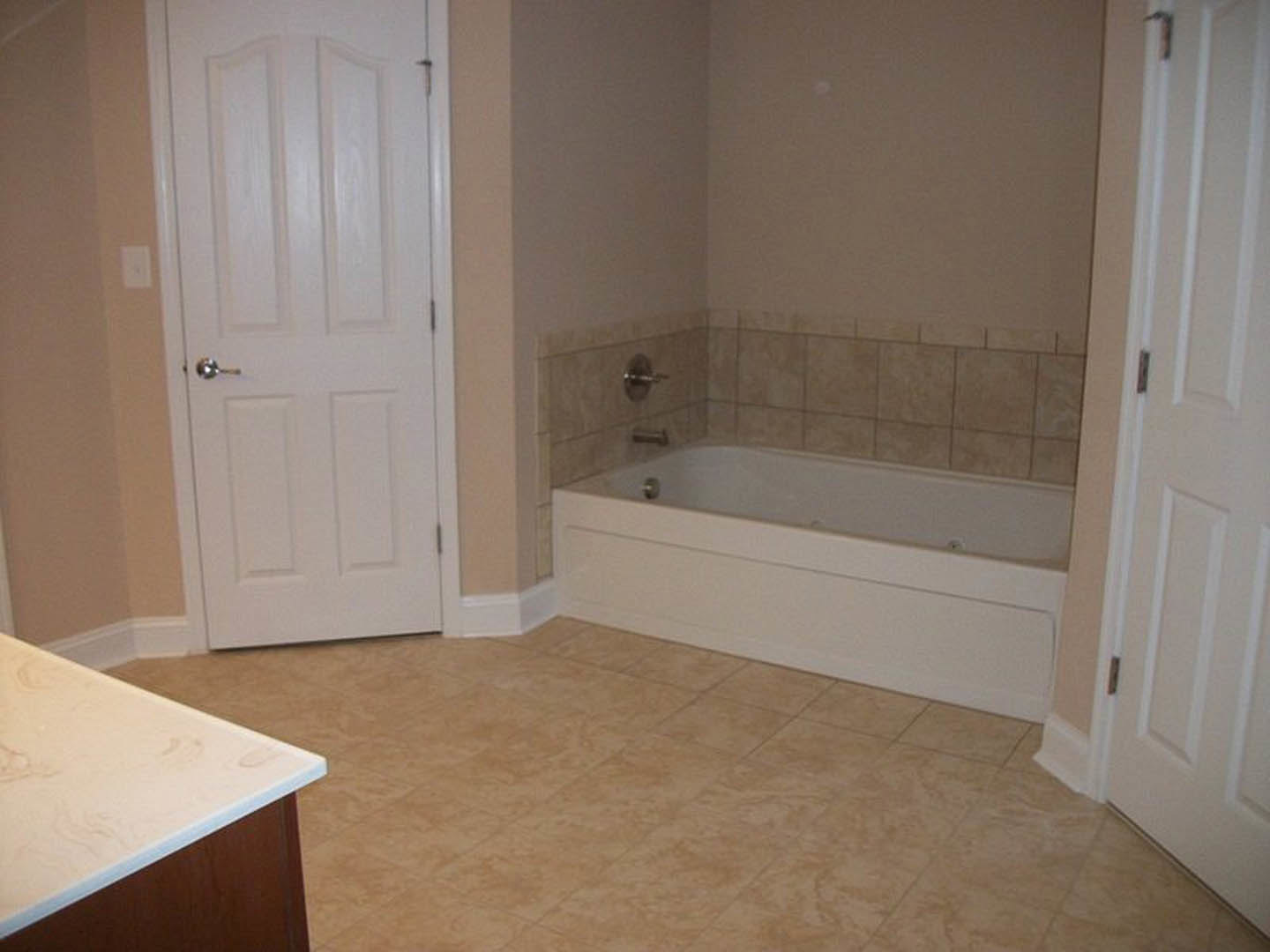 Modern bathroom featuring a freestanding white bathtub, sleek countertop with integrated sink, light tile flooring, and white paneled door with chrome hardware