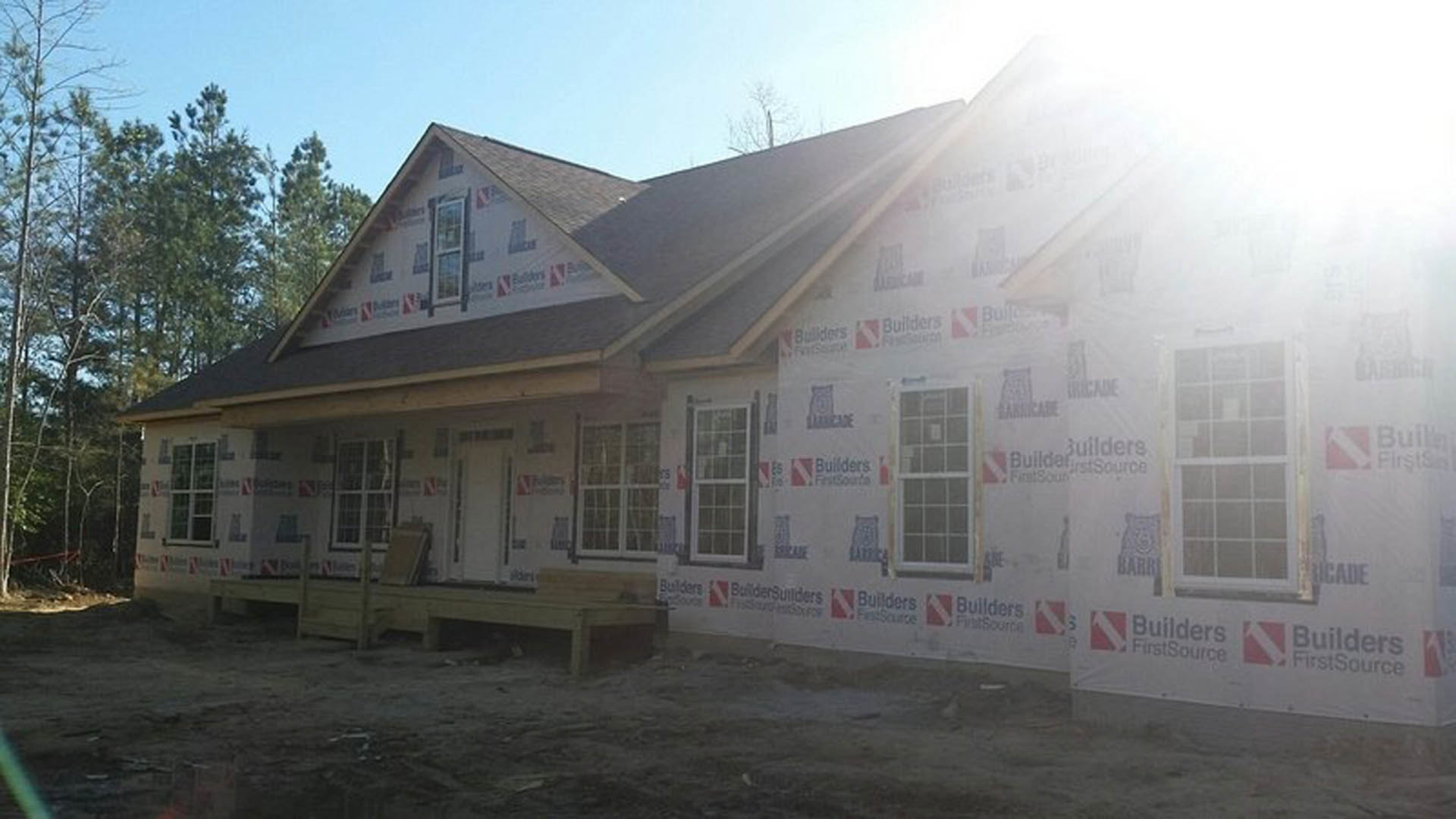 Partially built house with exposed insulation panels, white-framed window, sunlight illuminating exterior, trees visible in background