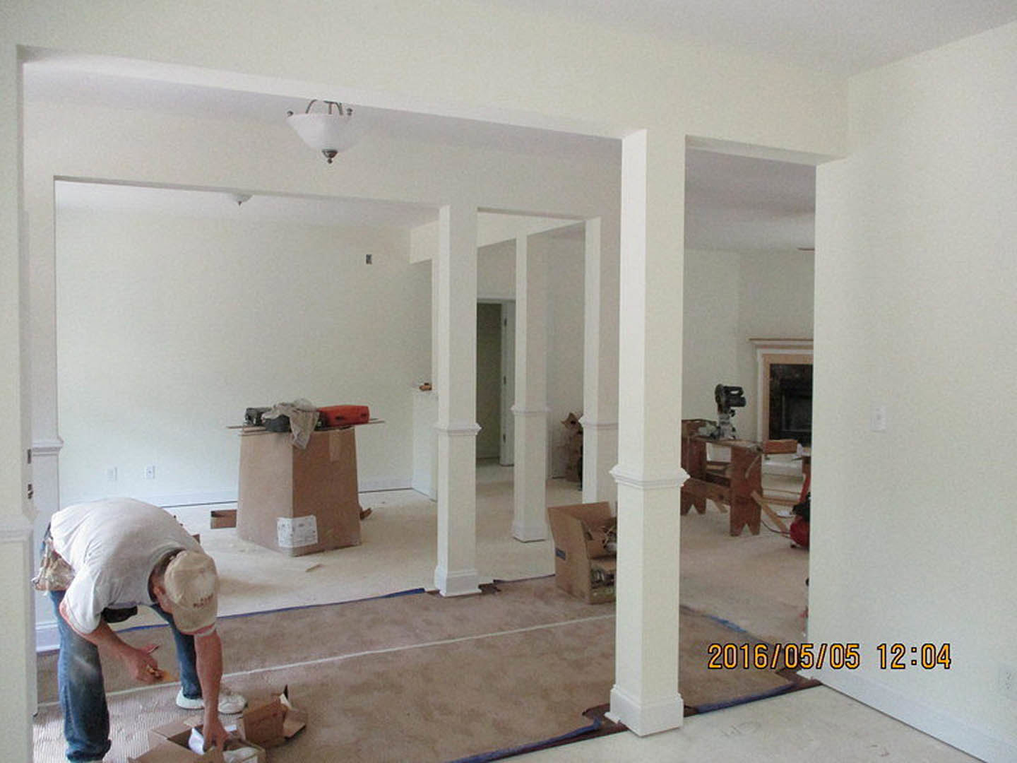 Man painting a white plaster wall beside a large mirror, cardboard box with white label on wood flooring, close-up of modern light fixture, white ceiling, and door in residential