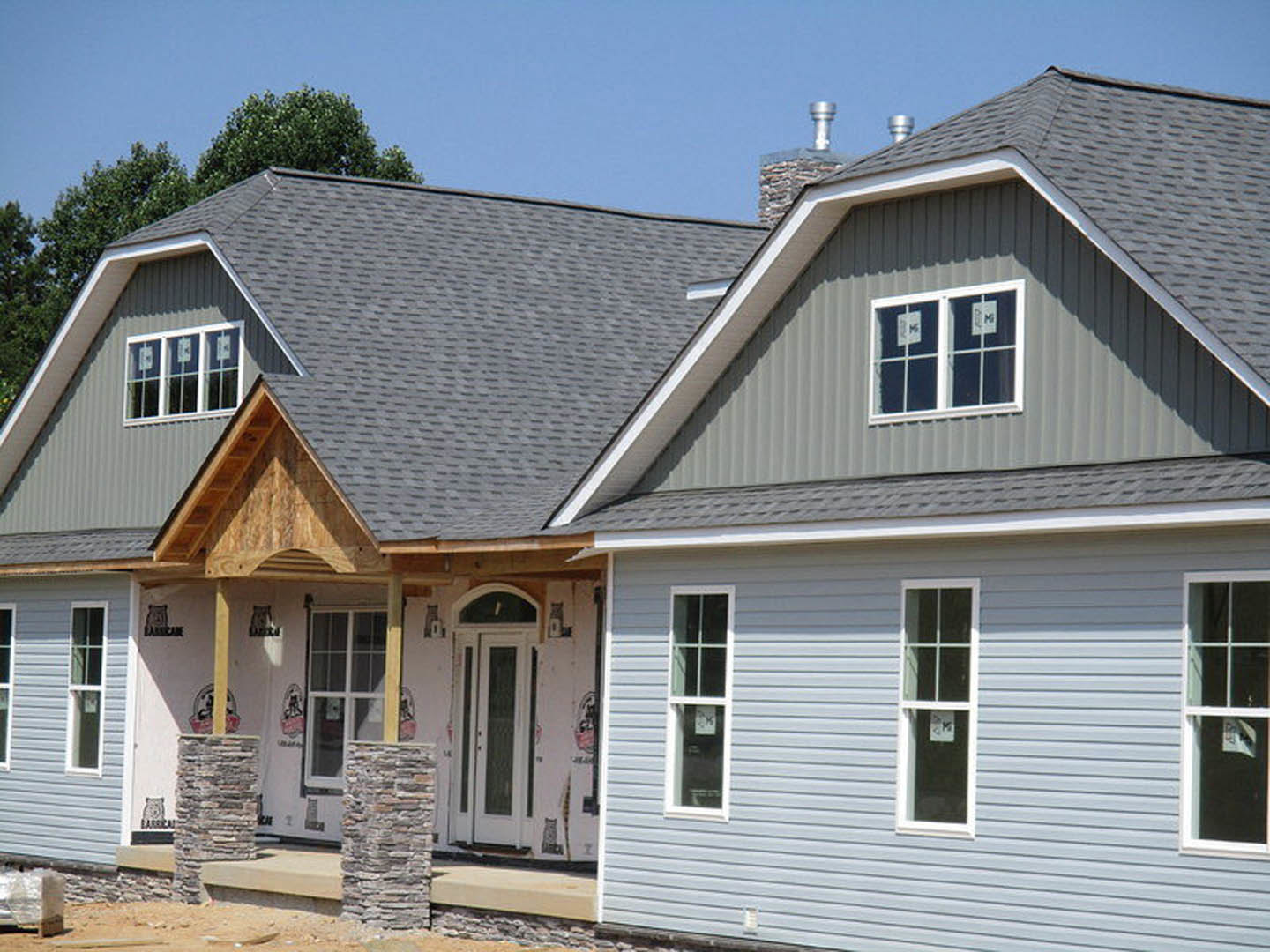 Two covered porches with stone pillars, white siding, sash windows, and a dark front door on a cottage-style home