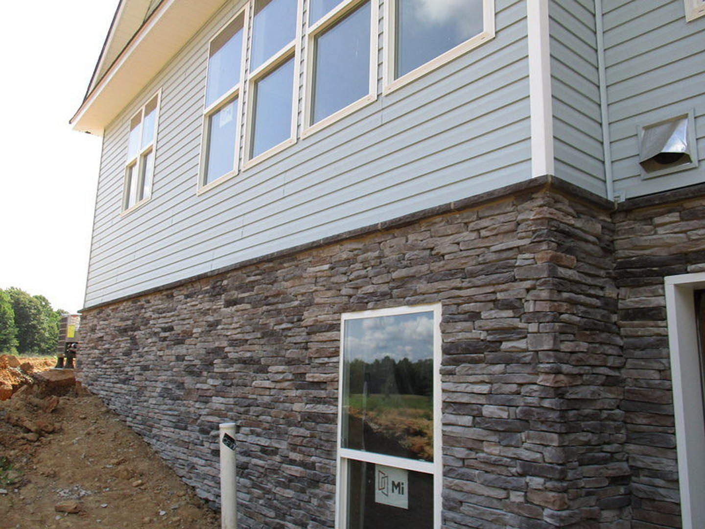 White siding home with large sash window, gray trim, and landscaped lawn under blue sky