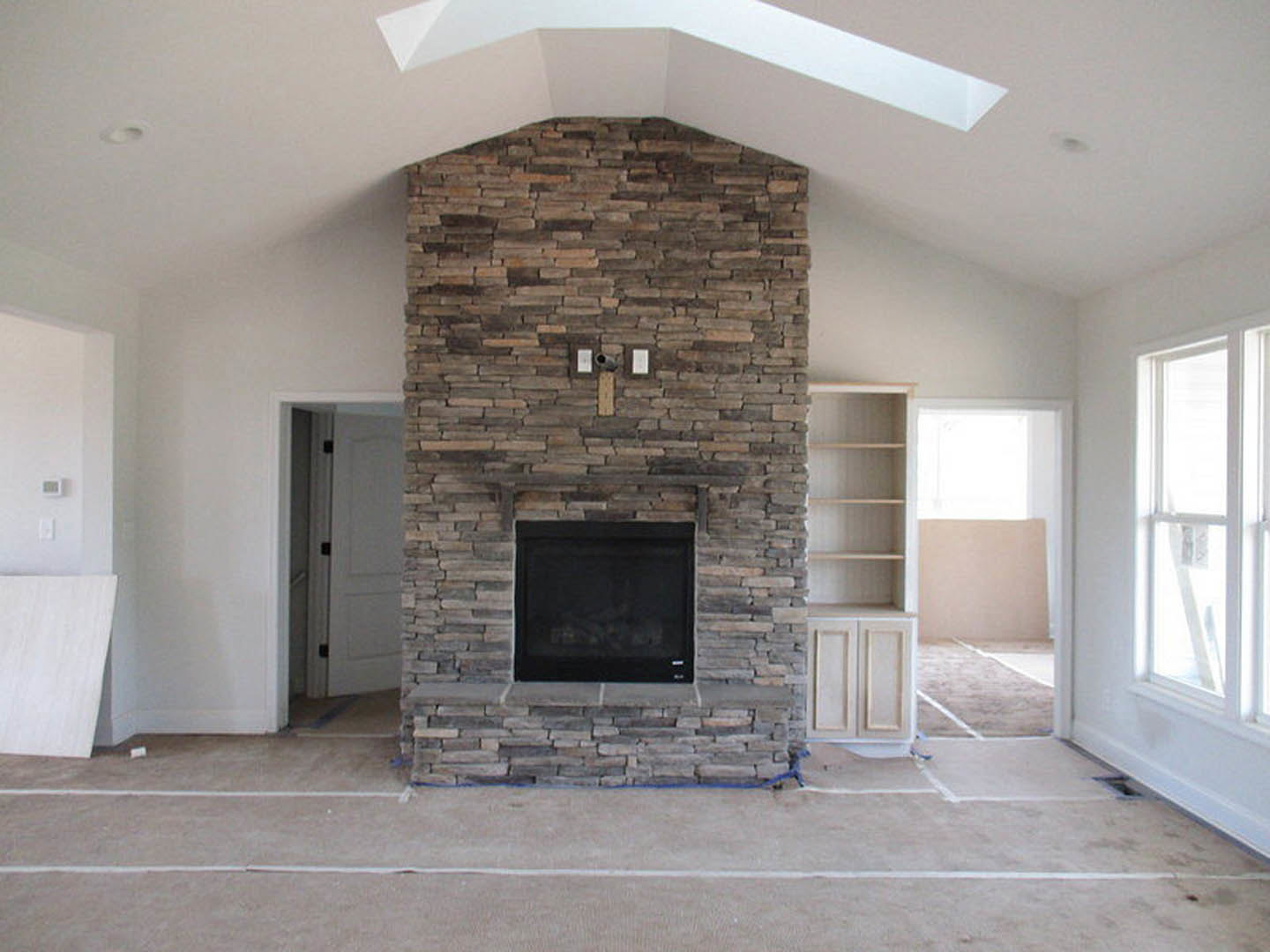 Black-framed fireplace set into a brick accent wall, white walls and ceiling, wood floor, window nearby