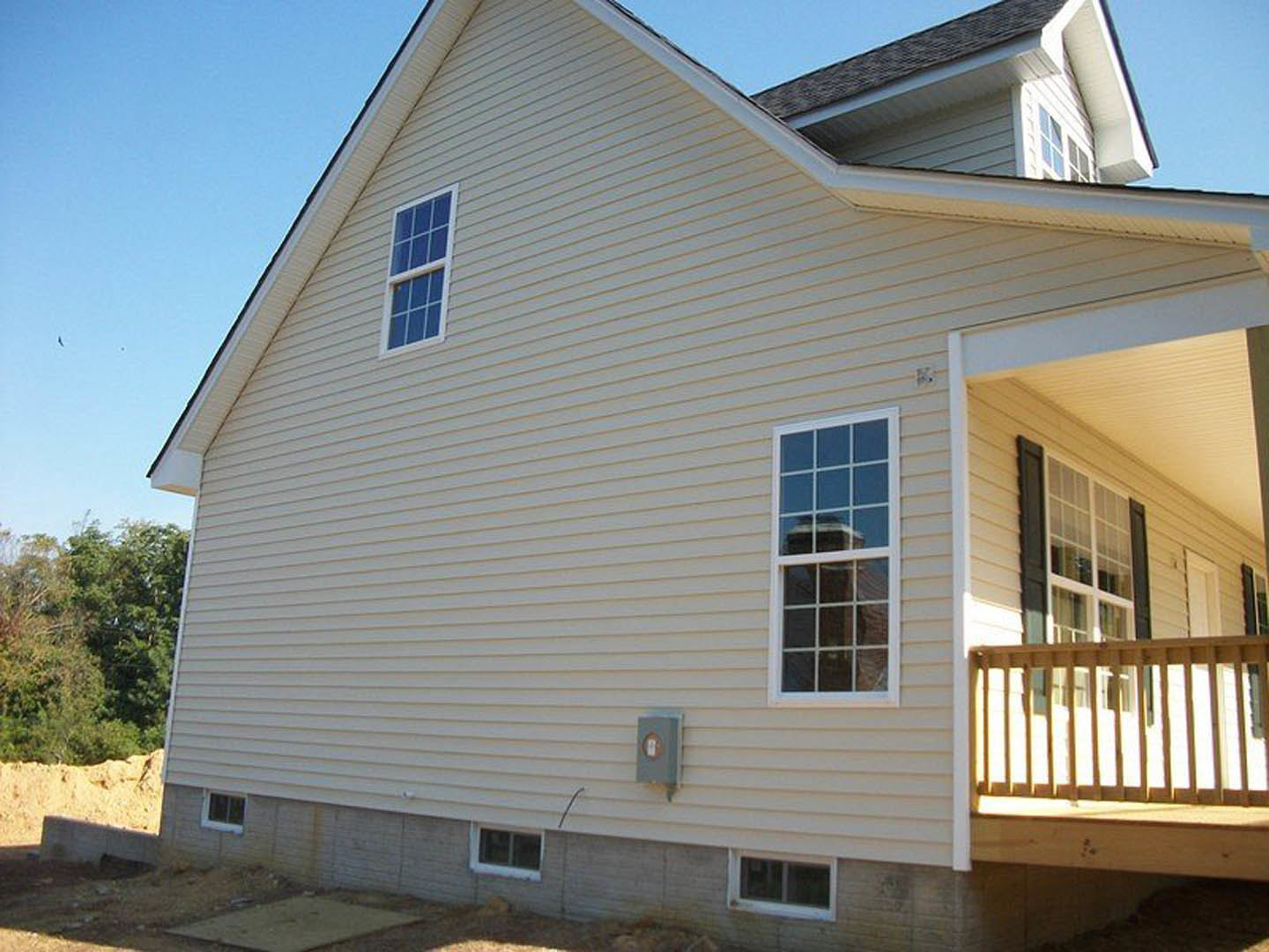 Two-story home with light siding, large windows, elevated wooden deck, and balcony overlooking landscaped yard with leafy tree