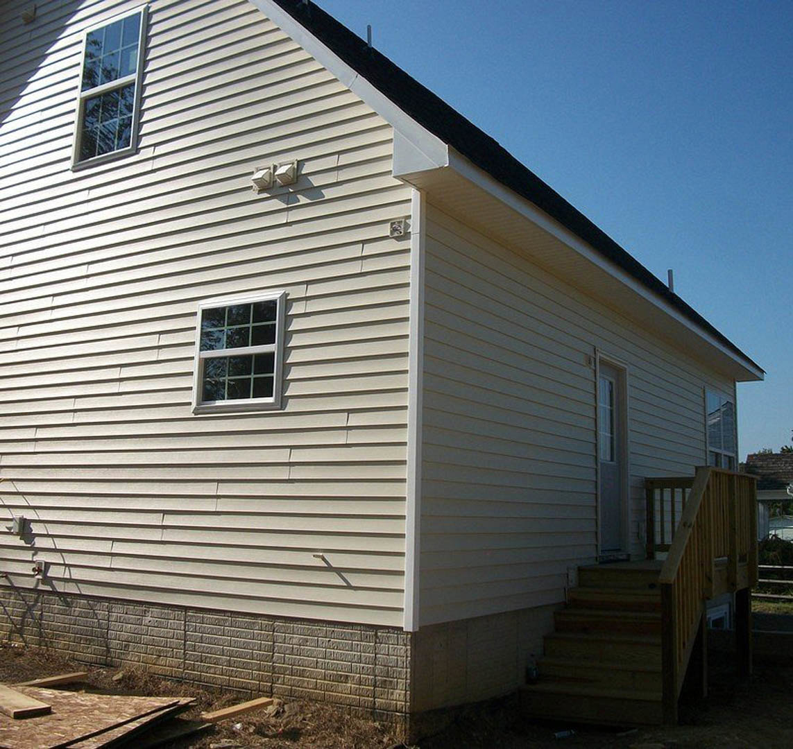 Two-story home with wood siding, large windows, and exterior wooden staircase leading to upper level; gabled roof and landscaped yard visible.
