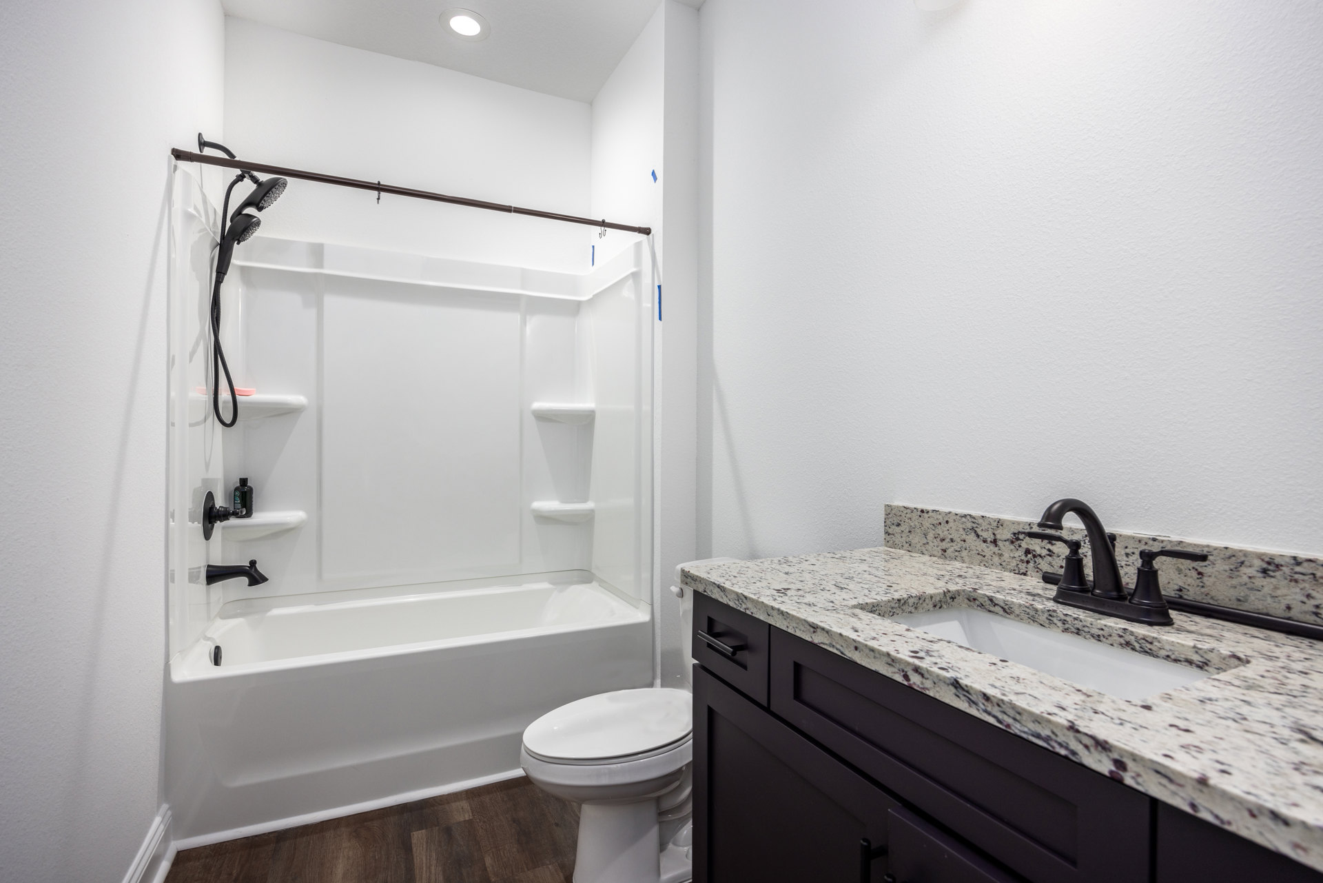 Bathroom with white bathtub featuring black faucets and handheld shower, white toilet with closed seat, white sink with black faucet, light tile walls, and wall-mounted mirror.