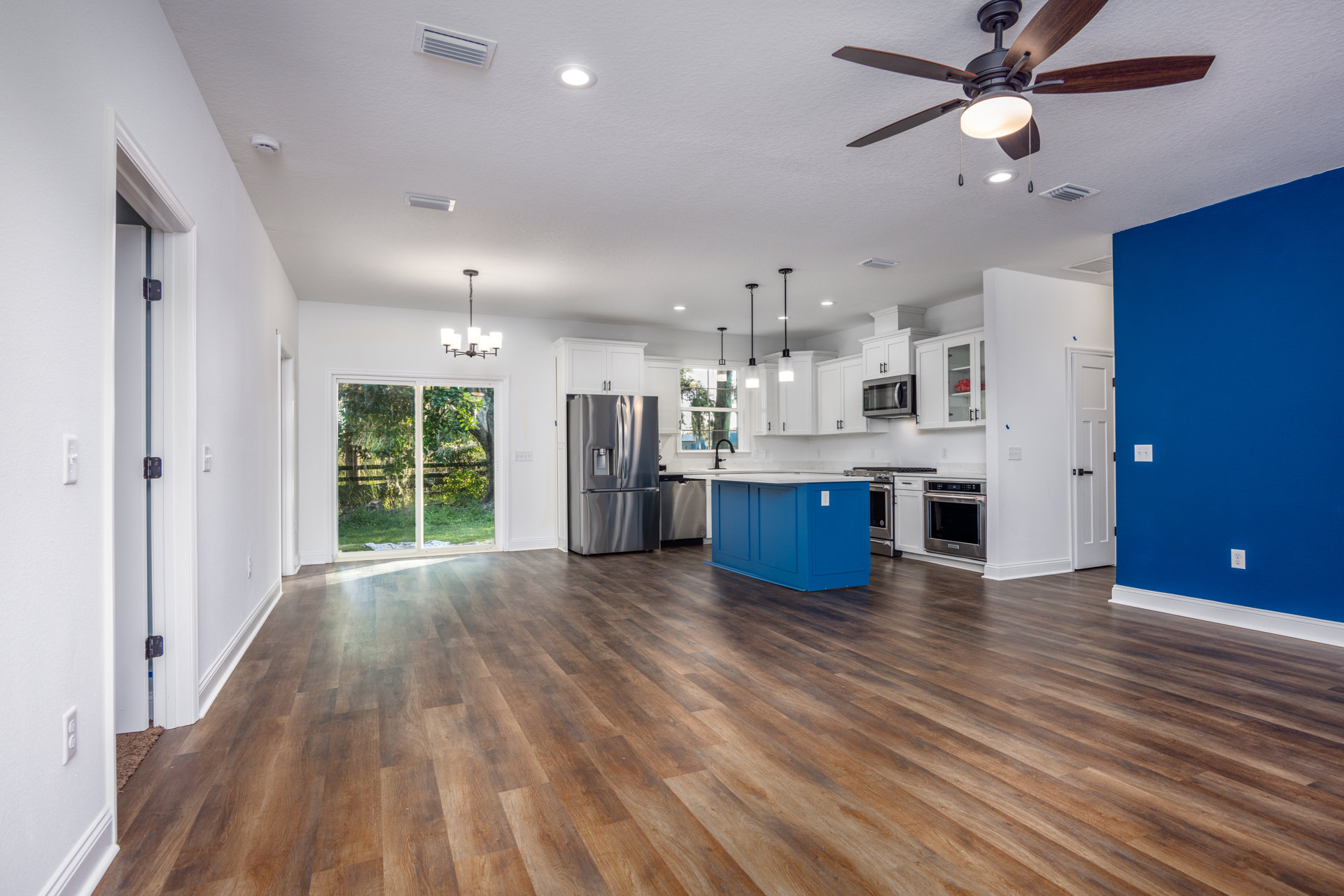 Spacious open floor plan featuring wood flooring, blue kitchen island with white countertop, blue cabinets, stainless steel refrigerator, microwave oven, and ceiling fan with light