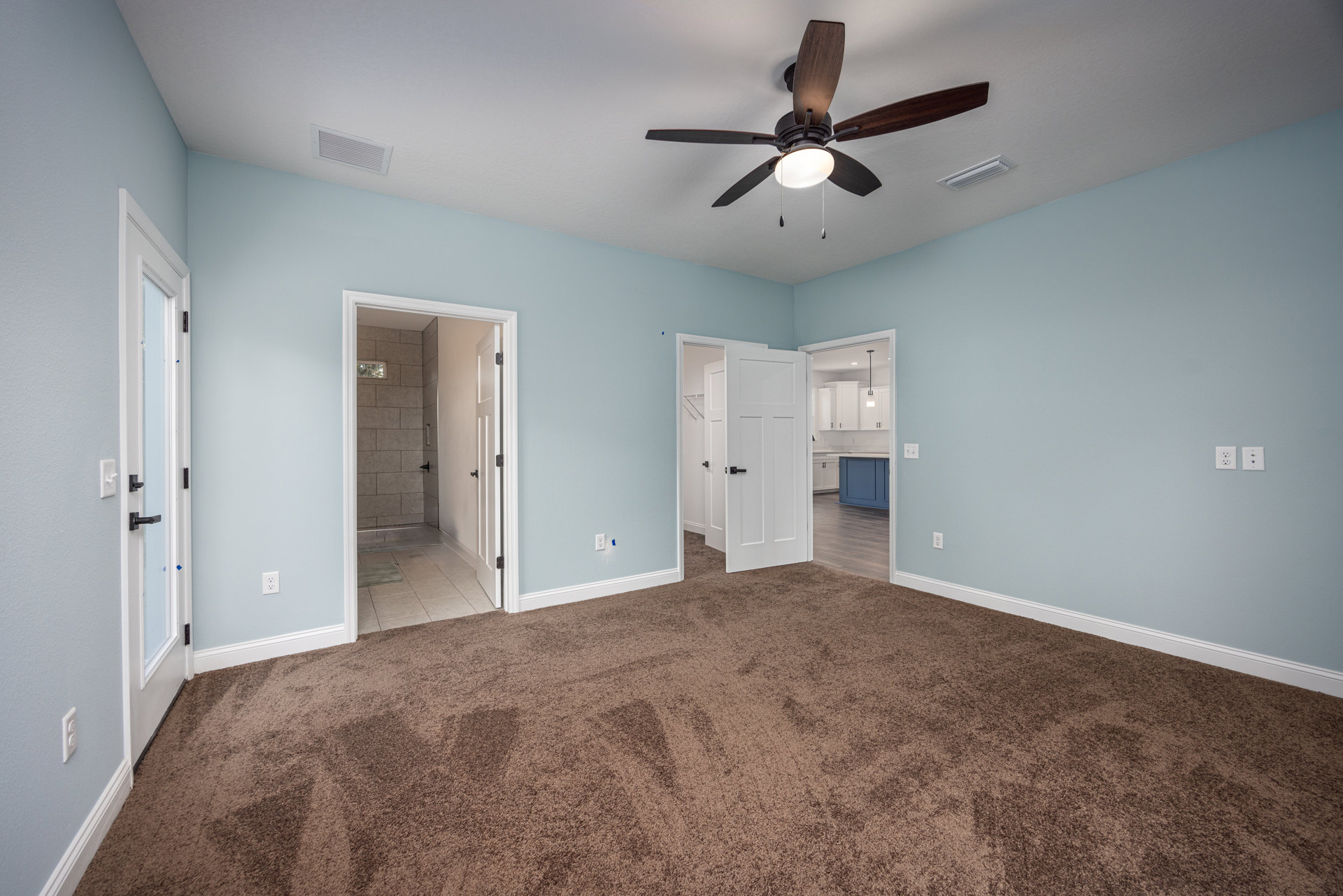 Ceiling fan with light fixture, brown carpet flooring, open door revealing tiled shower, white closet door with black handles, ceiling vent, neutral walls