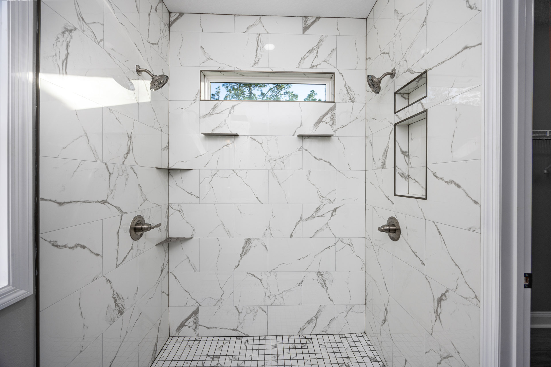 Marble shower walls with a rectangular window, chrome shower head, and tile floor