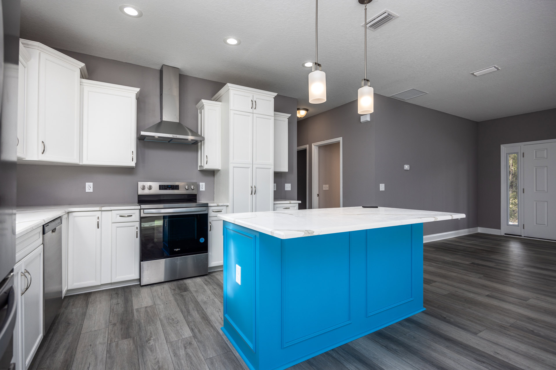 Blue kitchen island with white marble countertop, stainless steel oven with glass door, white cabinetry, pendant light fixture, white door with window, hardwood flooring