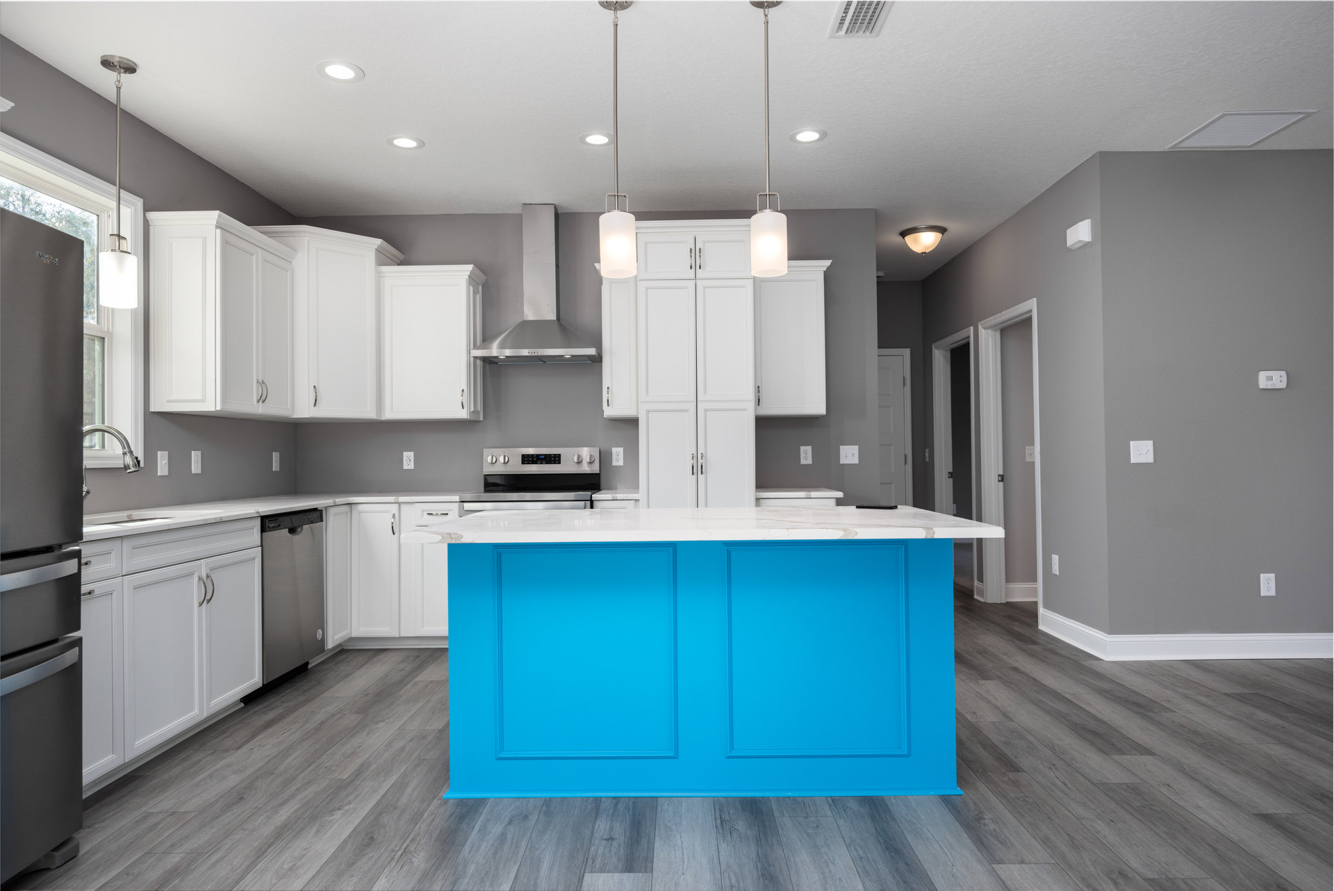 Blue kitchen island with white quartz countertops, black refrigerator, white pendant light fixture, light wood cabinetry, and stainless steel sink.