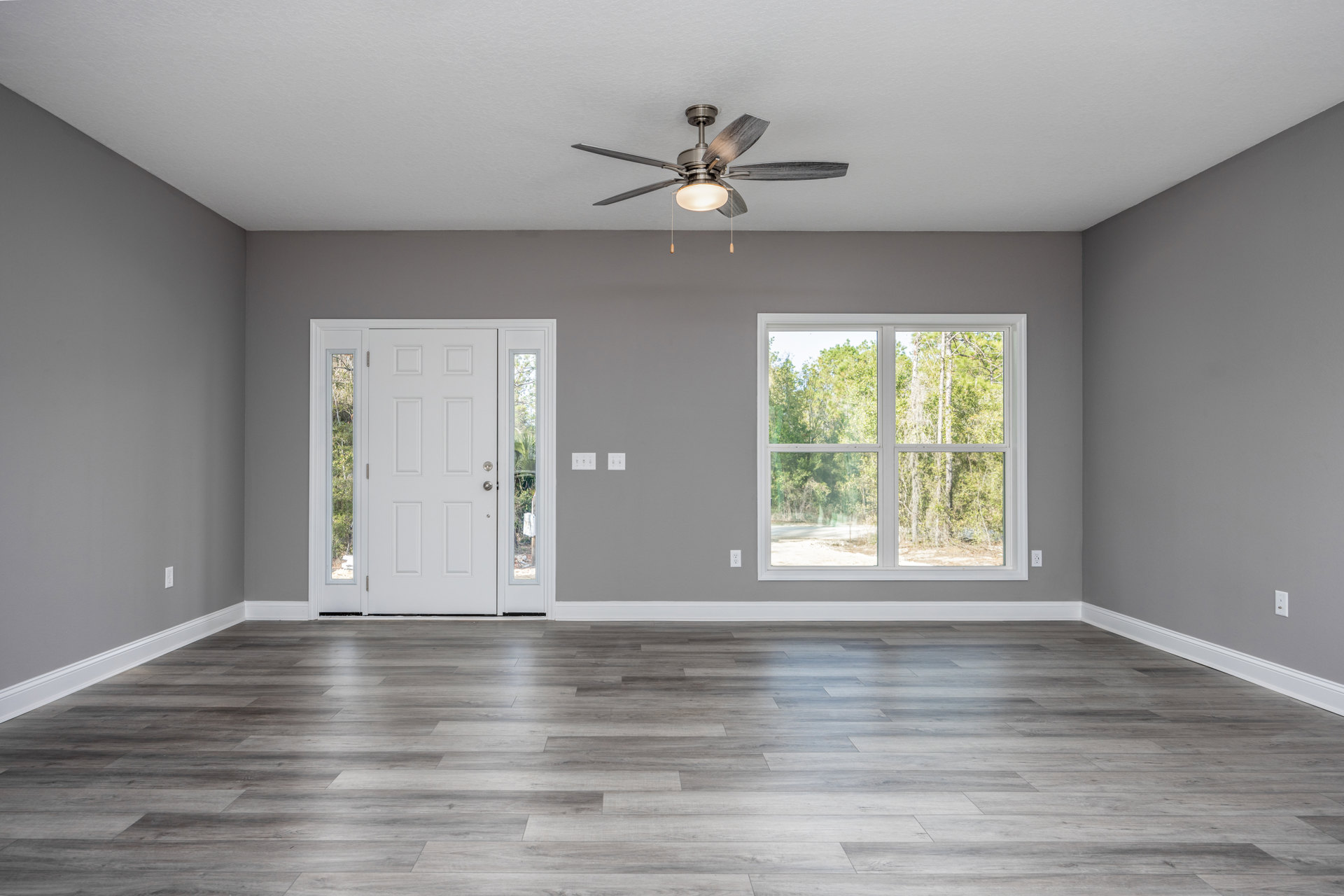 Ceiling fan with light fixture above wood laminate flooring, white door with glass panes open to reveal window view of trees outside