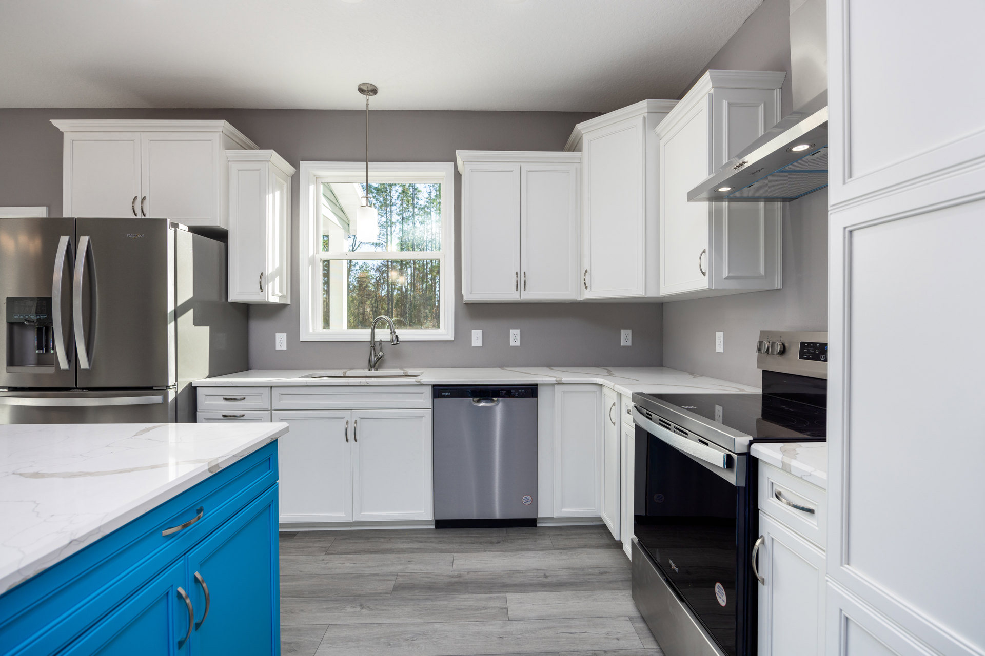 White kitchen cabinets with blue countertops, stainless steel dishwasher, white marble island with blue base cabinets, window with natural light, silver refrigerator, black and