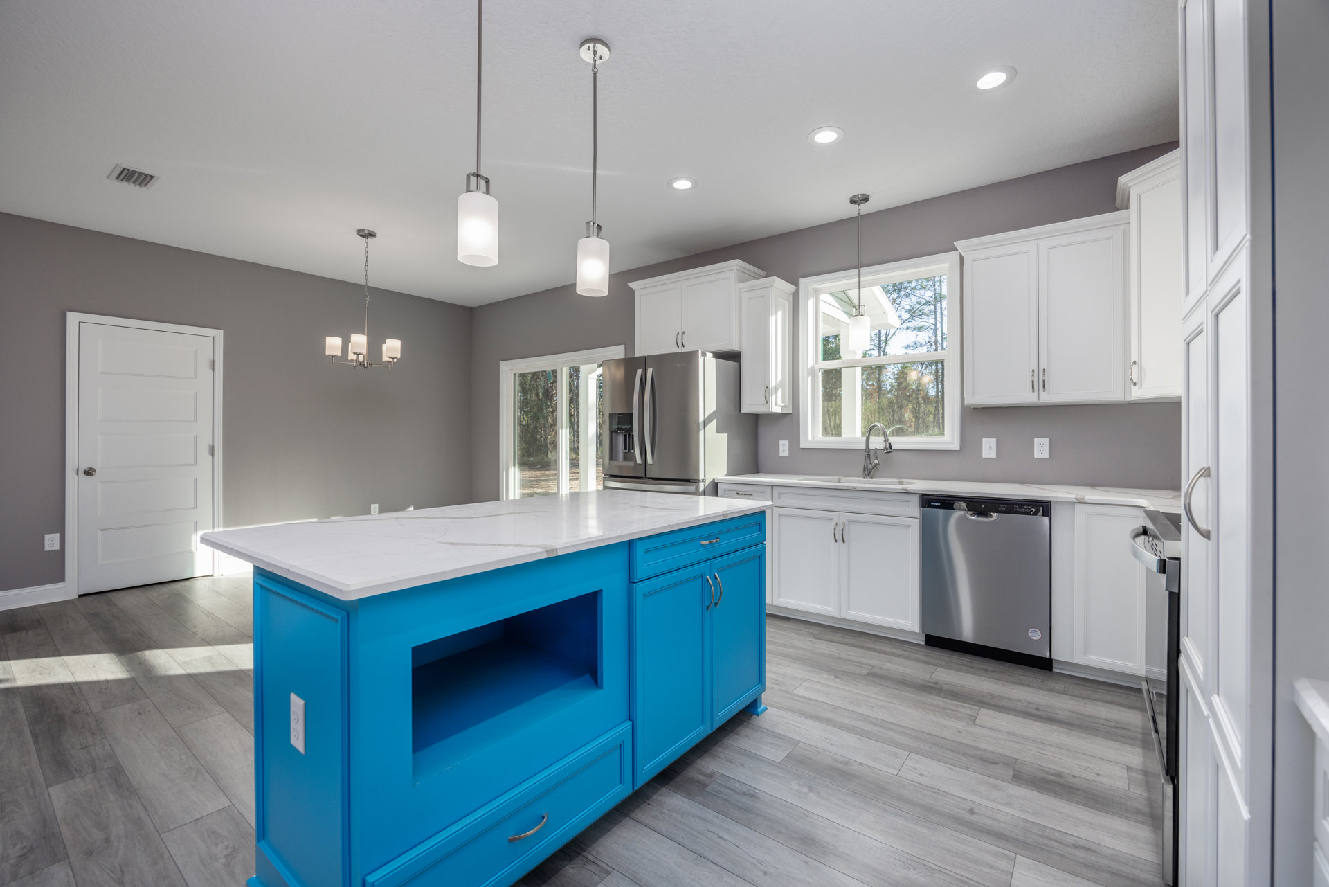 Blue kitchen island with white countertop, stainless steel dishwasher with black handle, white cabinetry, white door with silver handle, silver flagpole with red and white flag