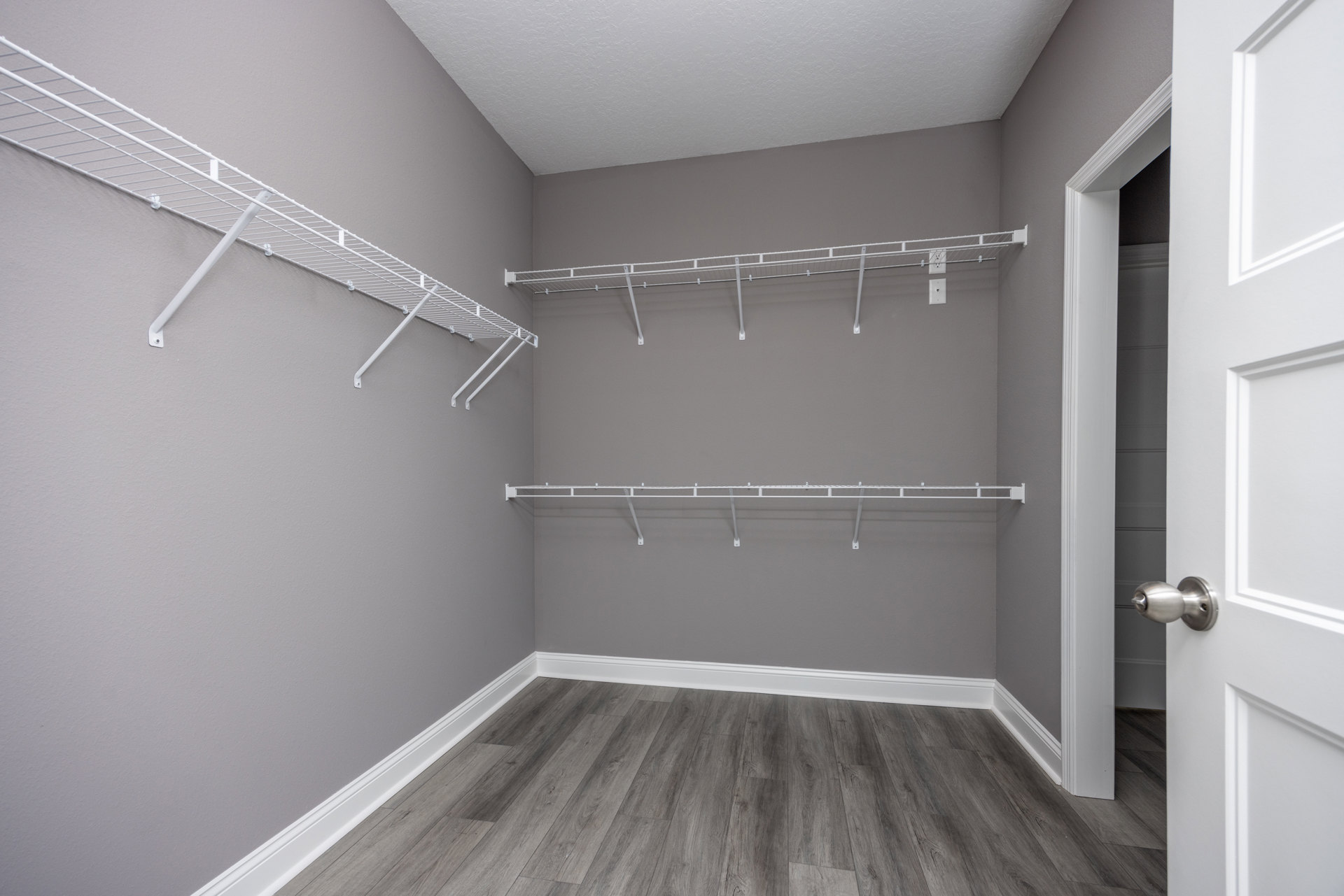 White built-in shelves on a plaster wall, wood flooring with white baseboard, close-up of a brushed metal door knob on a white door