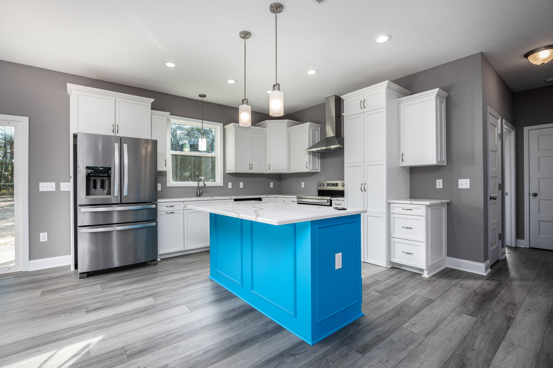 Blue kitchen island with white quartz countertop, white cabinetry with black trim, stainless steel refrigerator, light wood flooring, recessed ceiling lights, and built-in sink.