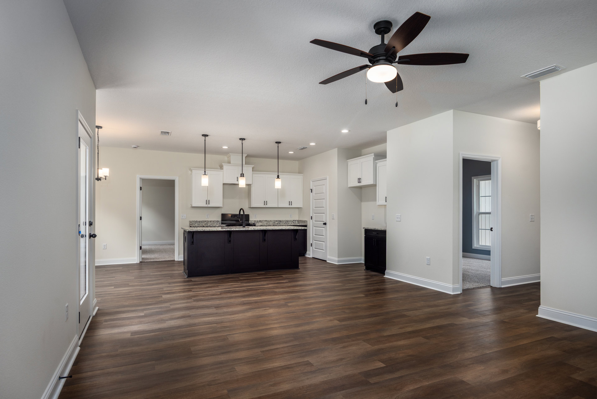 Large open kitchen featuring a ceiling fan with light, black countertop and faucet, white door with black handle, white walls, dark wood floors, and spacious kitchen island within