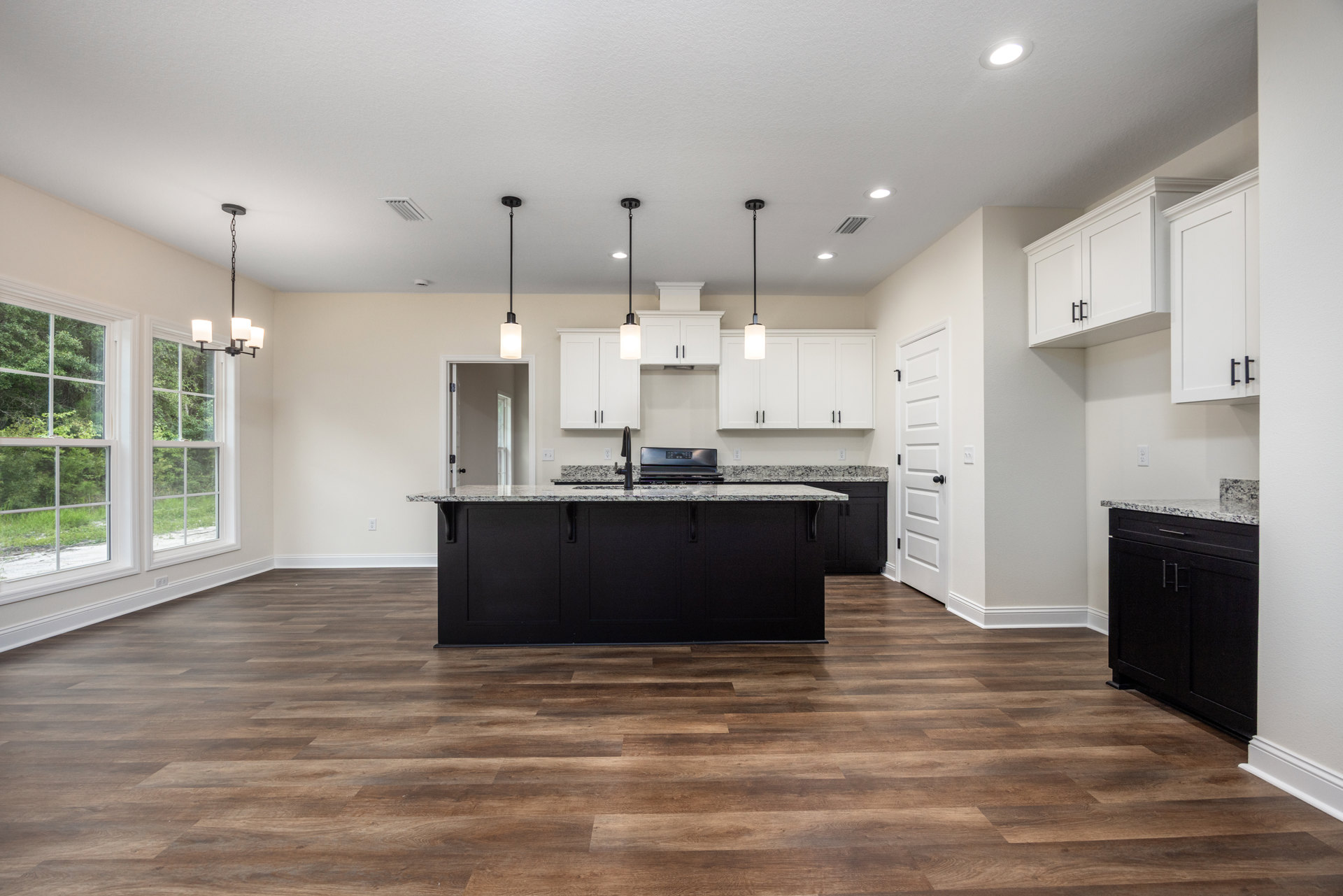 Spacious kitchen featuring a large black island with integrated sink, black cabinetry with matching handles, white door with black knob, modern stove, ceiling light fixture, tile