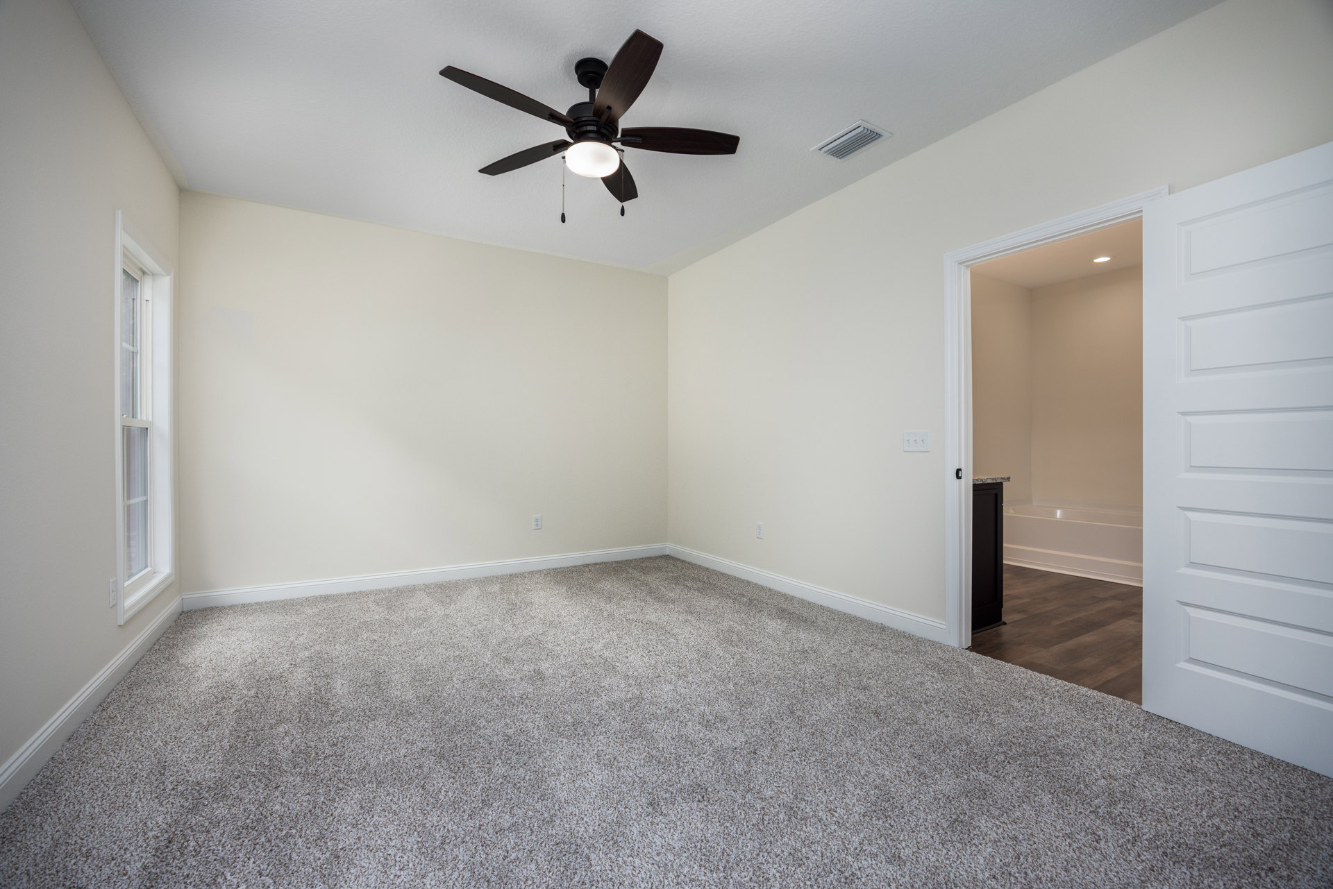 Carpeted room with white walls, ceiling fan with light fixture, white paneled door, and window letting in natural light