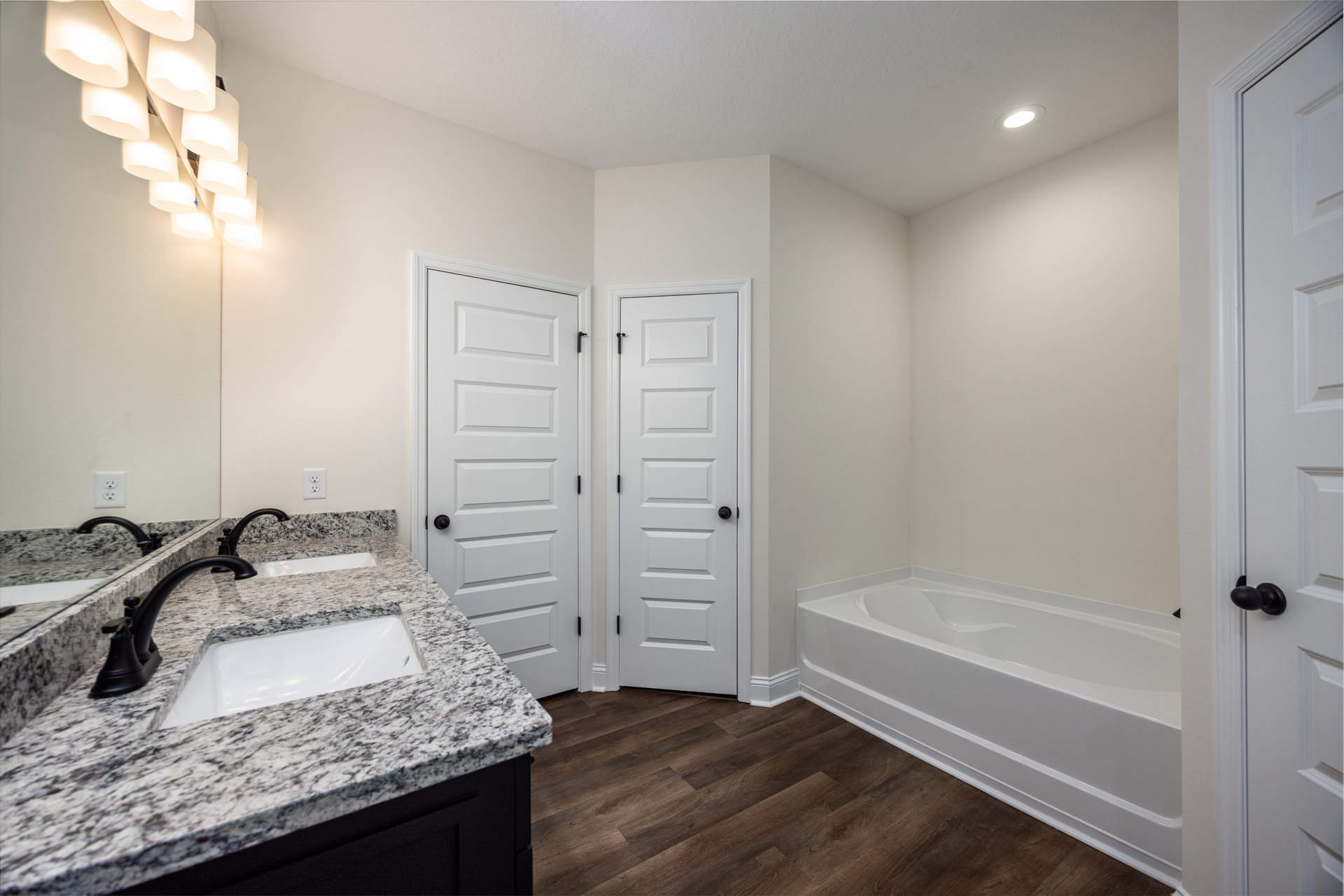 Bathroom featuring marble countertop with black faucet sink, freestanding white bathtub, white door with black knob, and ceiling-mounted group of lamps.