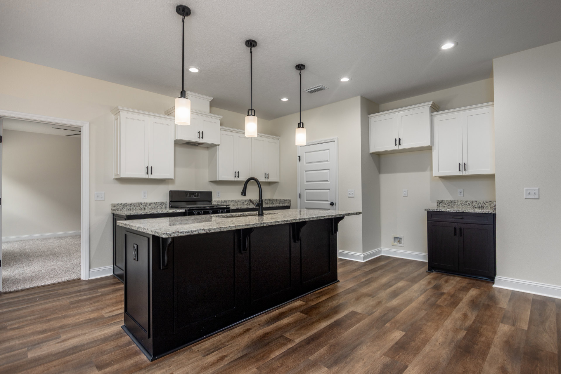 Kitchen featuring a black island with marble countertop, white cabinets with black handles, white tile backsplash, stainless steel sink, and light wood flooring
