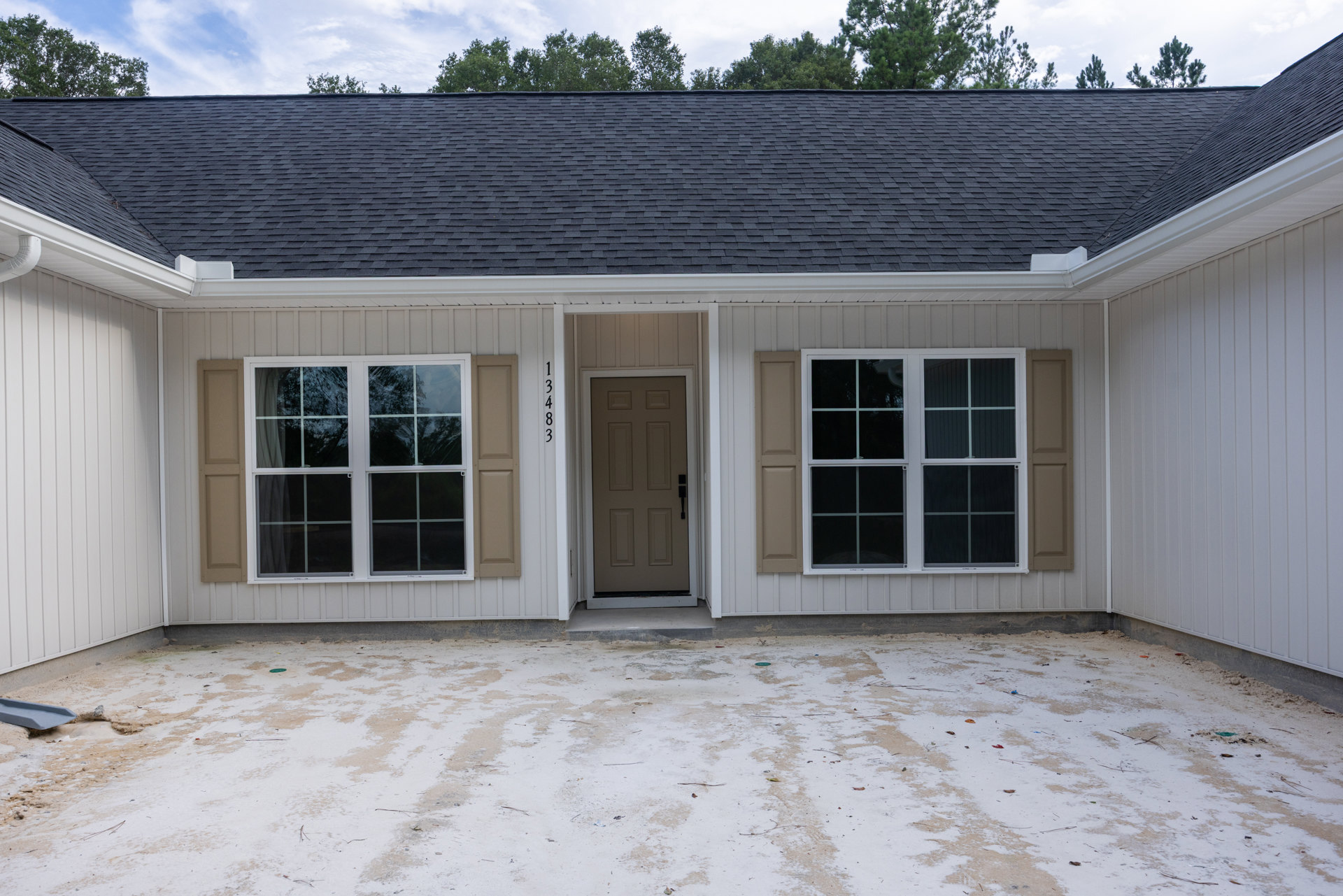 White front door with black handle, white-framed windows, snow-covered ground, blue sky, and leafless trees surrounding light-colored siding exterior