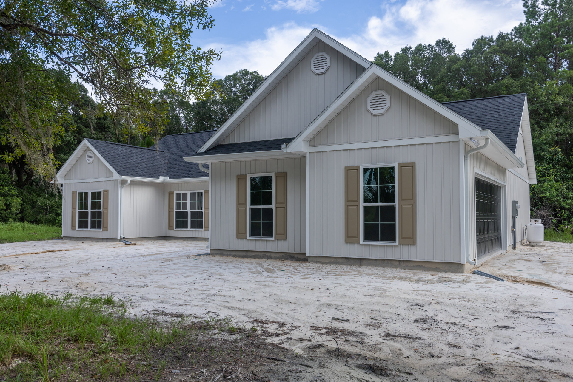 Two-story custom home with white siding, multiple windows including one with a broken pane, white vent on exterior wall, dirt road leading to entrance, surrounded by trees under