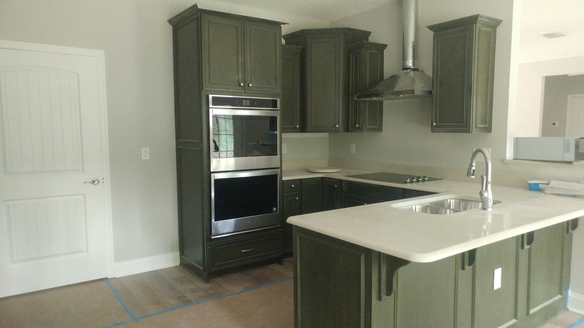 Green kitchen cabinets, stainless steel stove with oven window, white door with silver handle, built-in microwave, chrome faucet, and sink set in a light countertop
