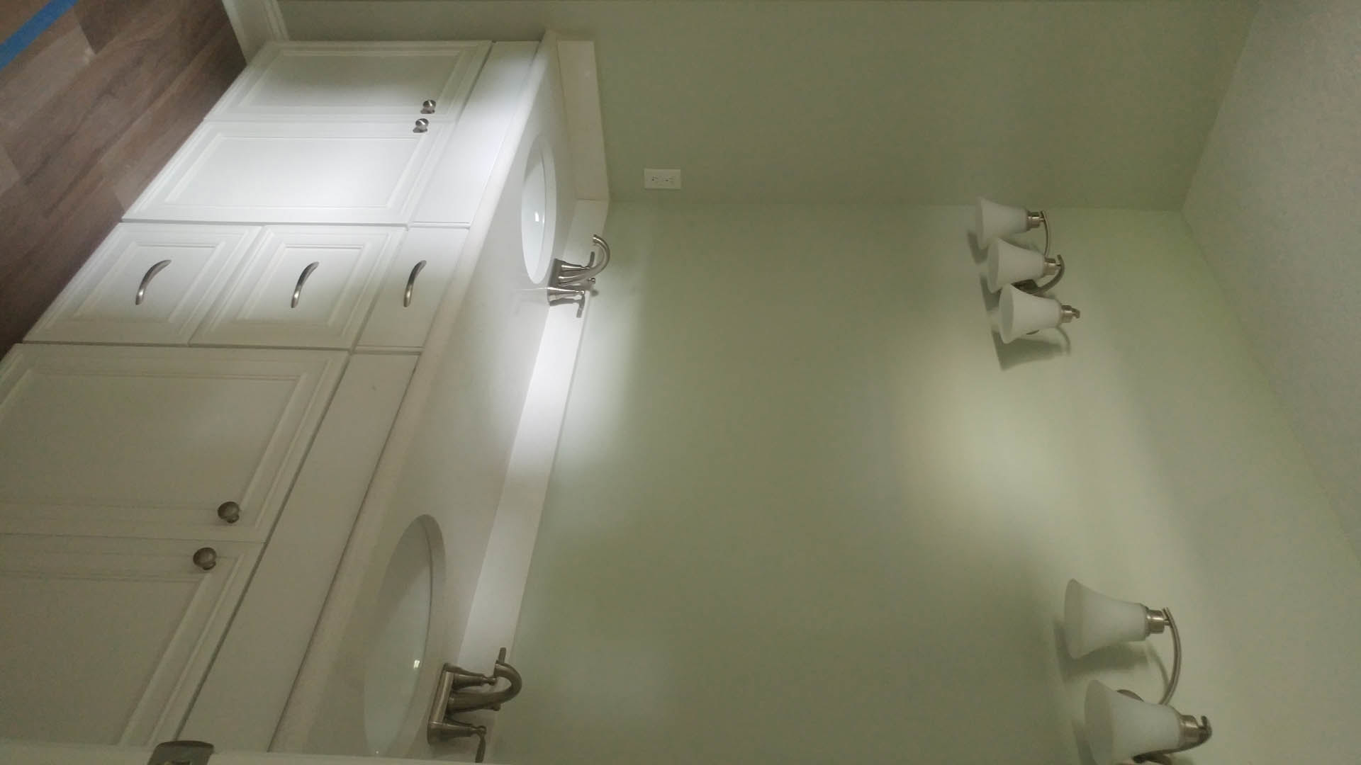 White bathroom cabinets with silver handles, white countertop and sink, wall-mounted light fixture, plaster walls, and tiled floor.