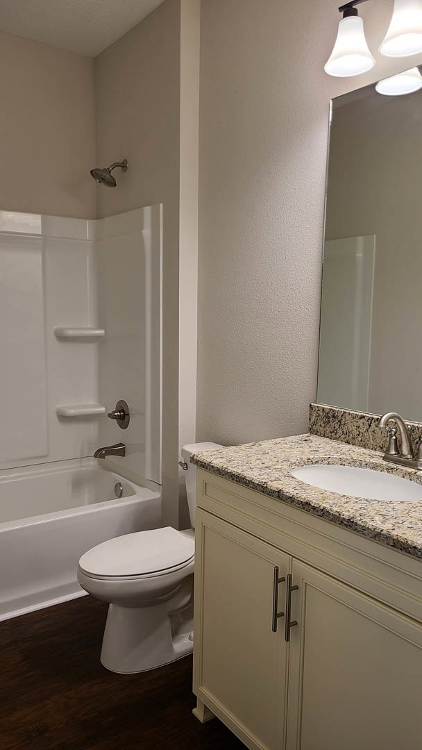 Bathroom with freestanding bathtub, marble-topped vanity with oval sink, chrome faucet, wall-mounted shower head, white toilet, and light fixture above tiled walls