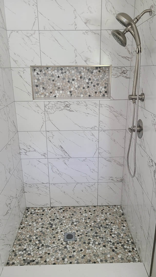 Walk-in shower with white tile floor, black and white stone accent wall, linear drain, handheld shower head, and contrasting white tile wall with black grout lines