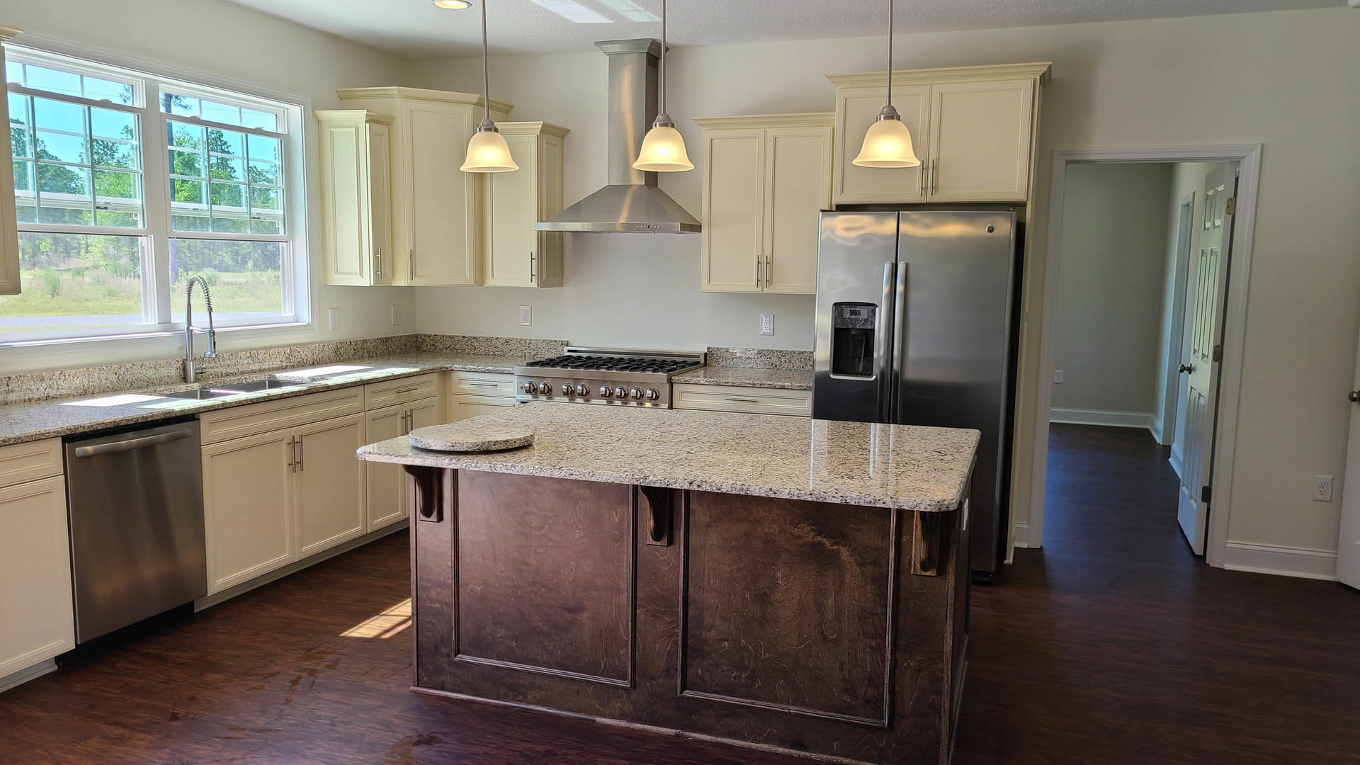 Kitchen featuring a large marble-topped island, stainless steel refrigerator, stove, dishwasher, white cabinetry, and a sink beneath a window