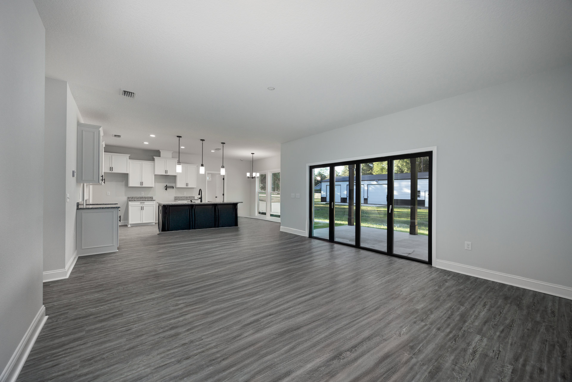 Open-concept kitchen with white cabinetry, marble countertops, black island with faucet, and wide sliding glass door overlooking green lawn