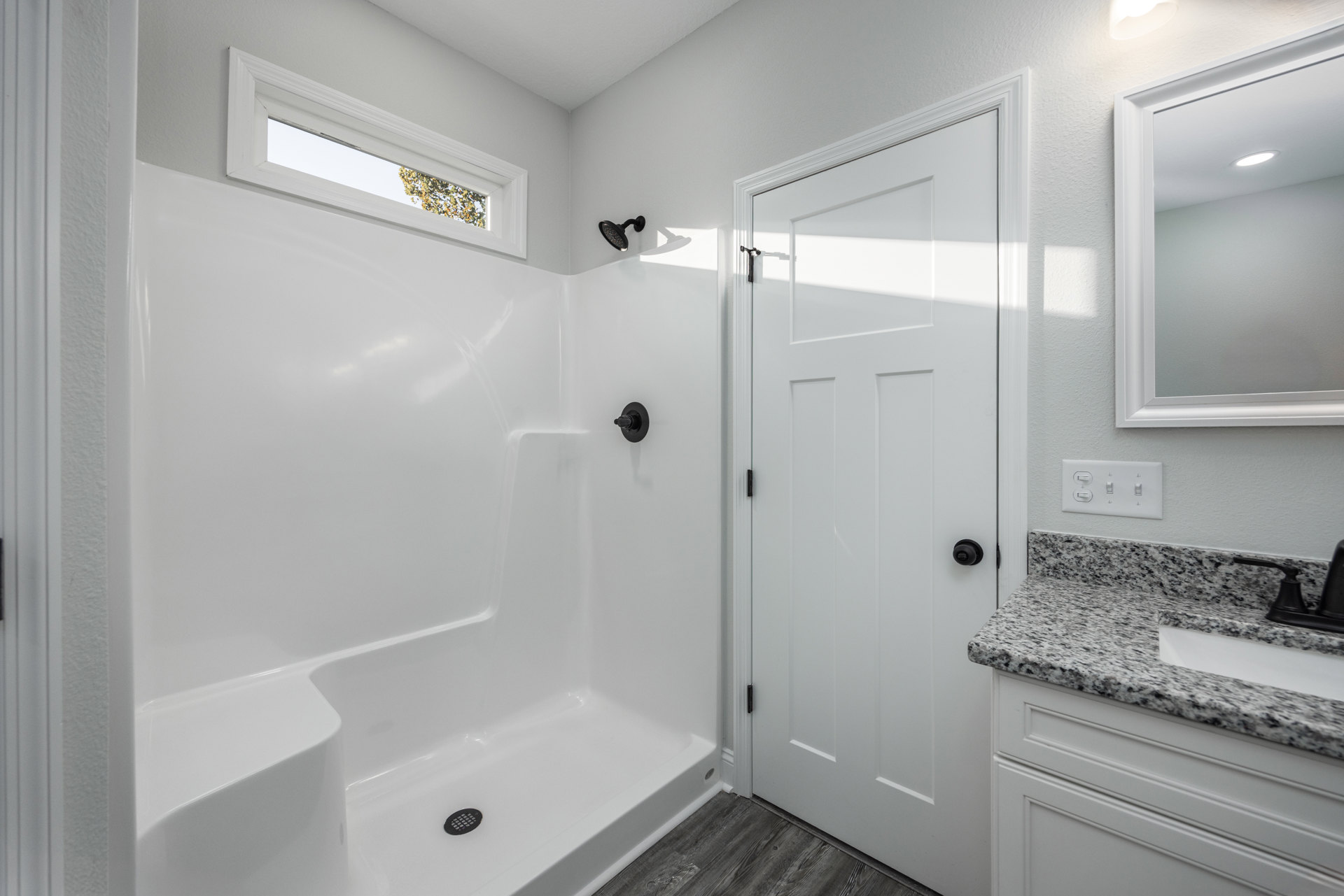 Modern bathroom featuring a white tiled shower with a window, chrome curved shower head, white sink, and black light switch on the wall
