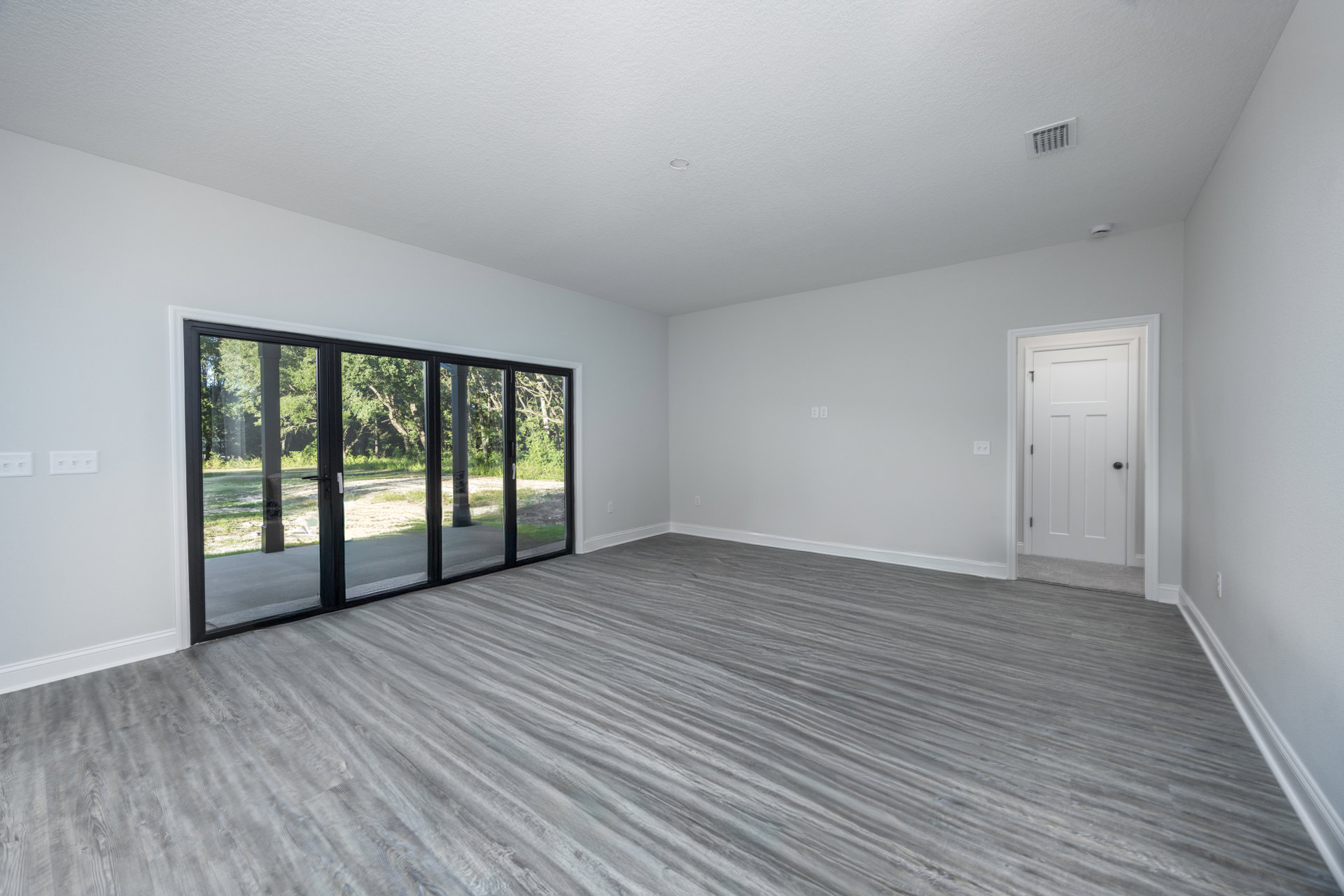 Room with wood flooring, white walls, sliding glass door framed in white, black door knob, wall vent visible.