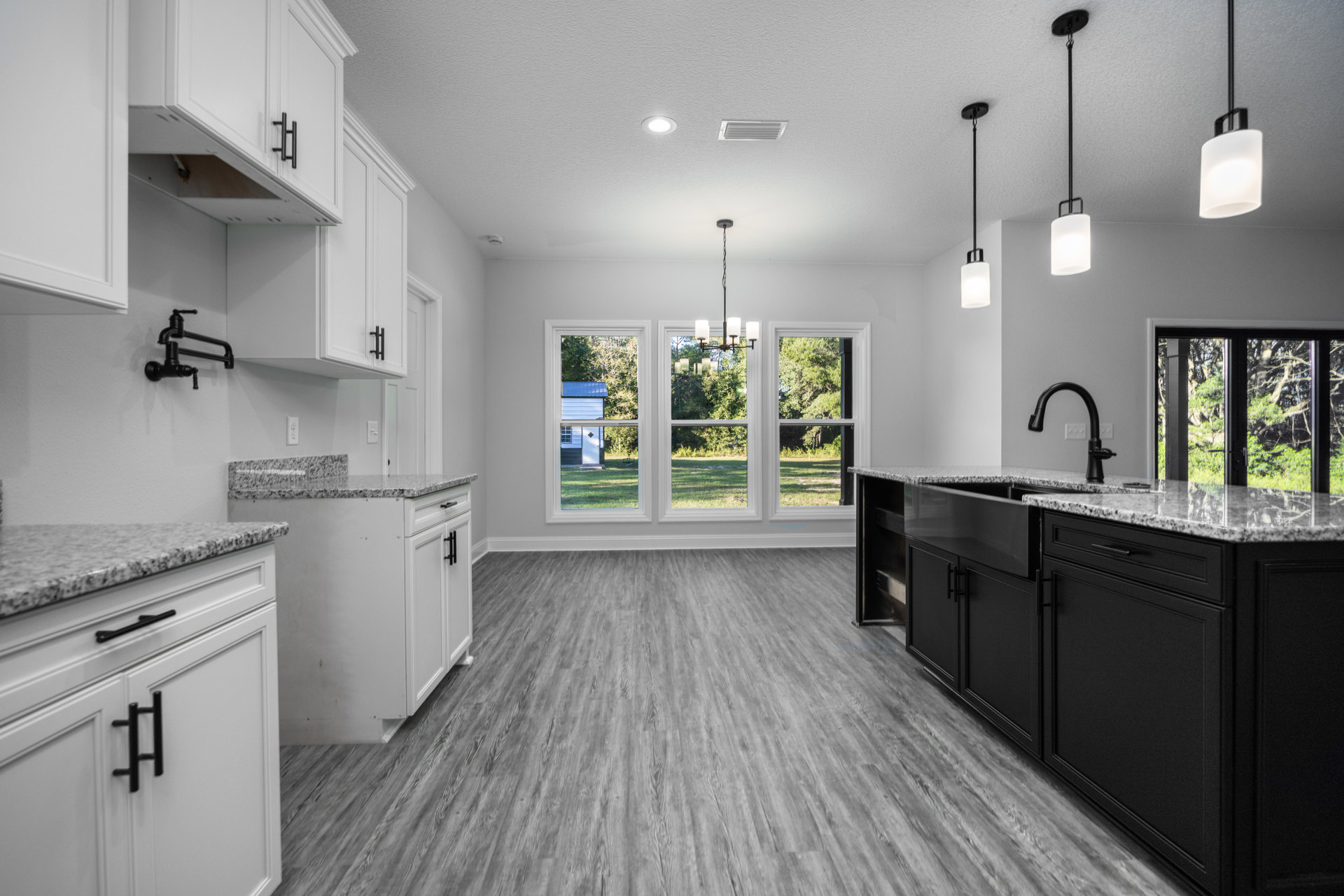 White kitchen with granite countertops, white cabinets, stainless steel sink beneath a window overlooking trees, white light fixture, black pencil on white countertop.