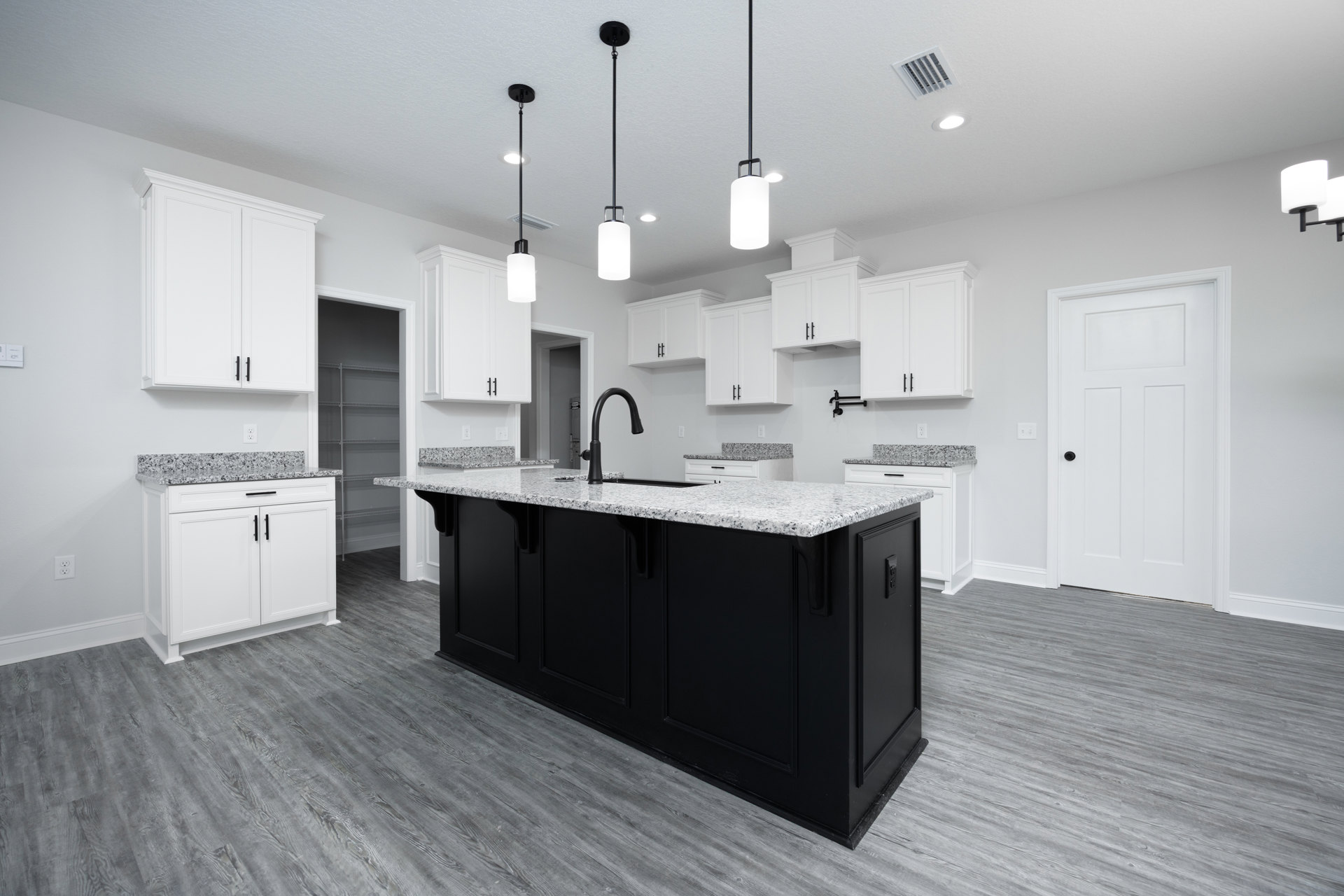Black kitchen island with waterfall countertop, surrounded by white cabinets with black handles, stainless steel sink, light wood flooring, and recessed ceiling lights.