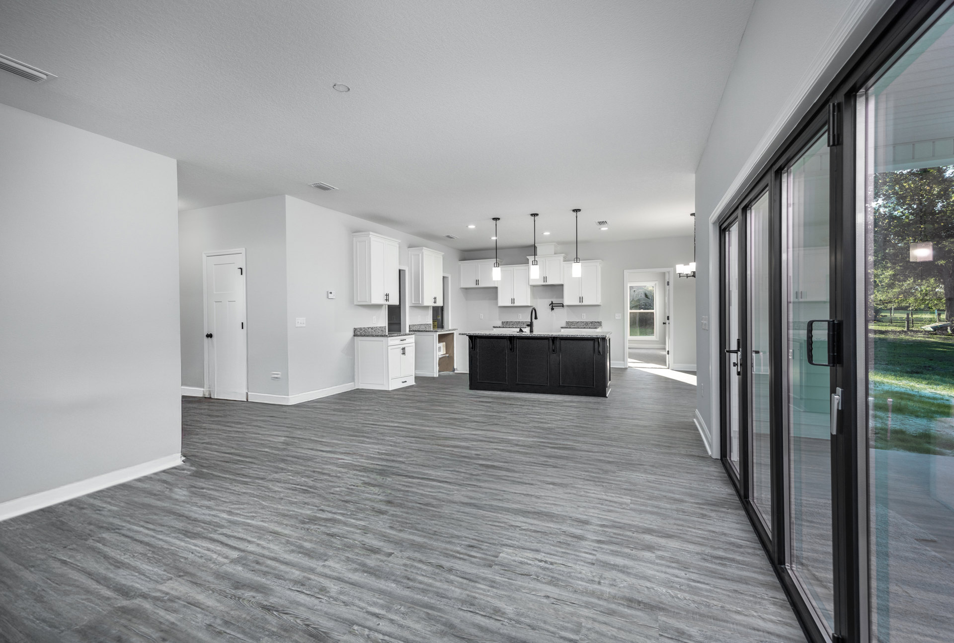 Open-concept kitchen with white cabinets, marbled countertops, black hardware, and sliding glass doors leading to outdoor space; white walls and light flooring throughout.