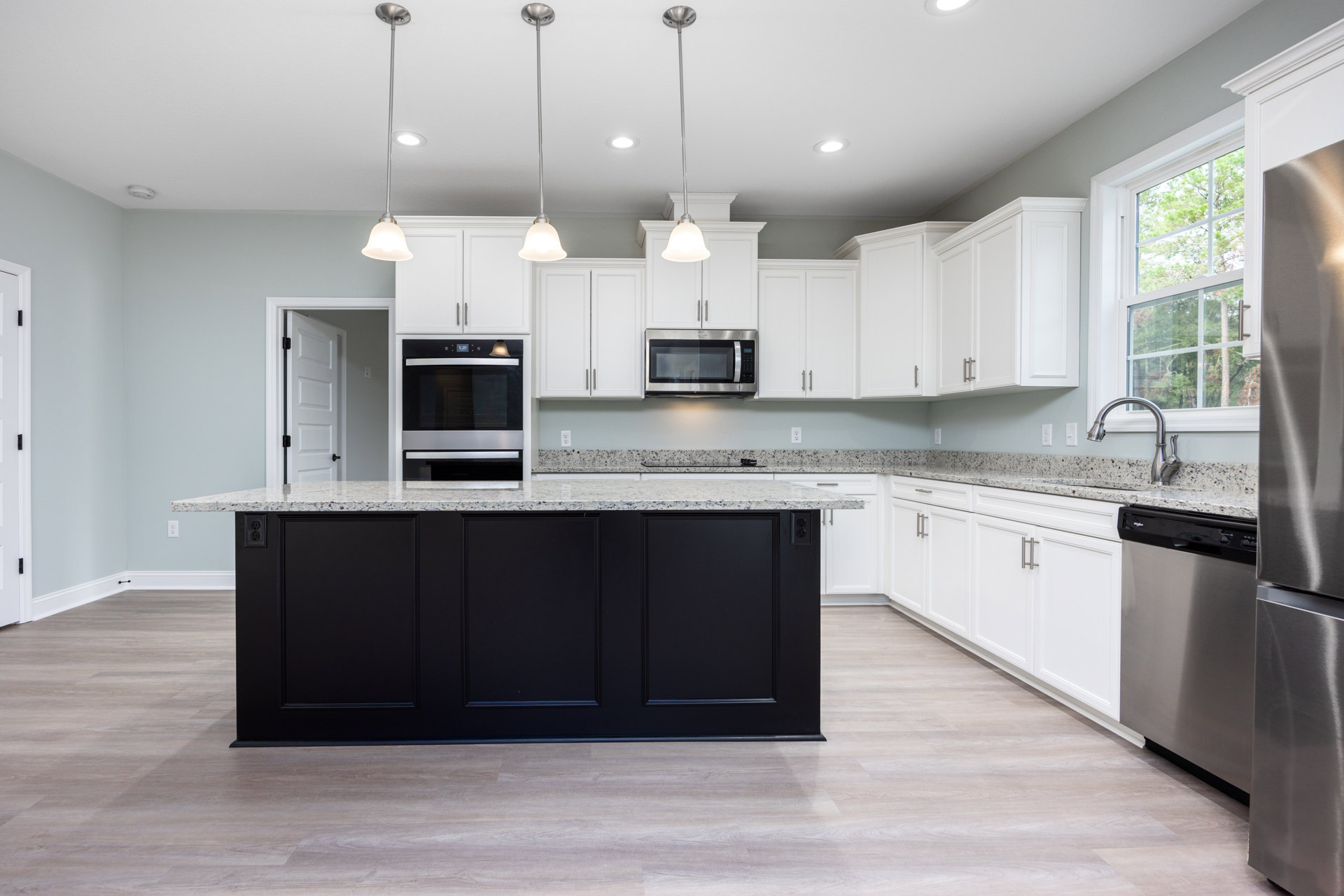 White kitchen with marble countertops, stainless steel microwave and oven, black lower cabinet, pendant light fixture hanging from ceiling