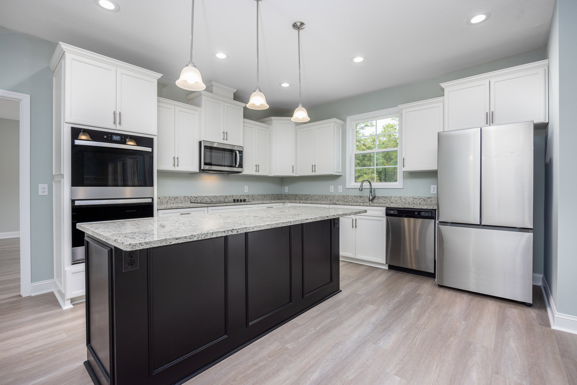 White kitchen cabinets with black appliances, including a silver refrigerator, open microwave, and black-and-silver dishwasher, white countertops, light flooring, and neutral