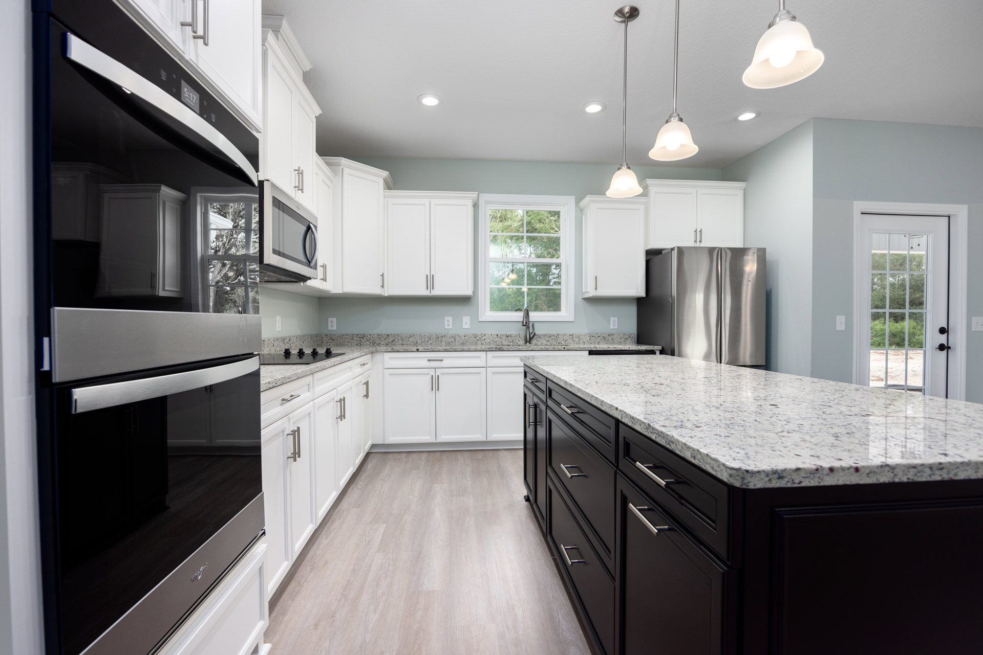 White kitchen cabinets, black appliances, stainless steel refrigerator, black lower cabinets, white-framed window, white ceiling, slim metal rod, modern light fixture with exposed