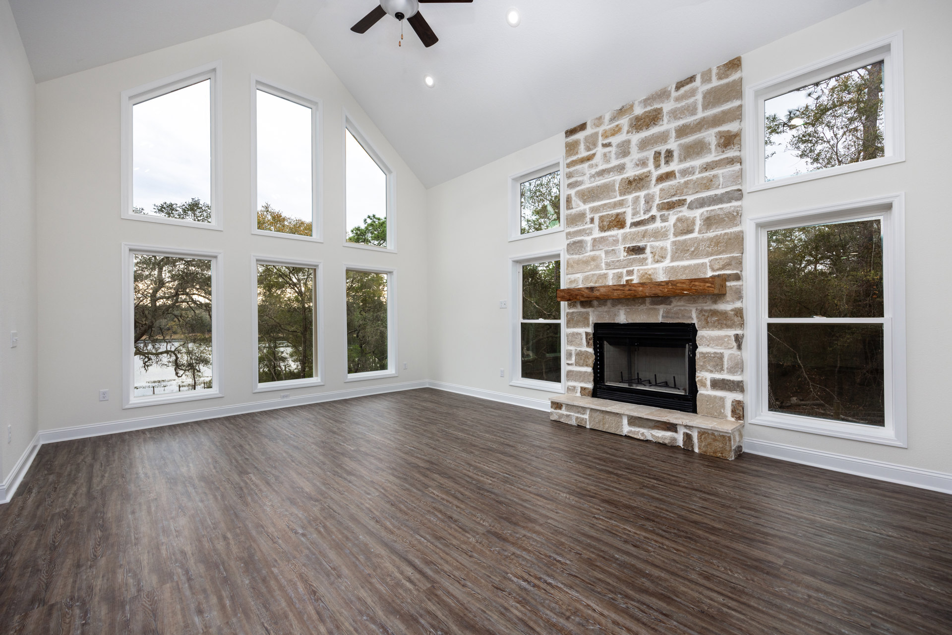 Living room with hardwood floors, black-framed fireplace, white window overlooking trees and water