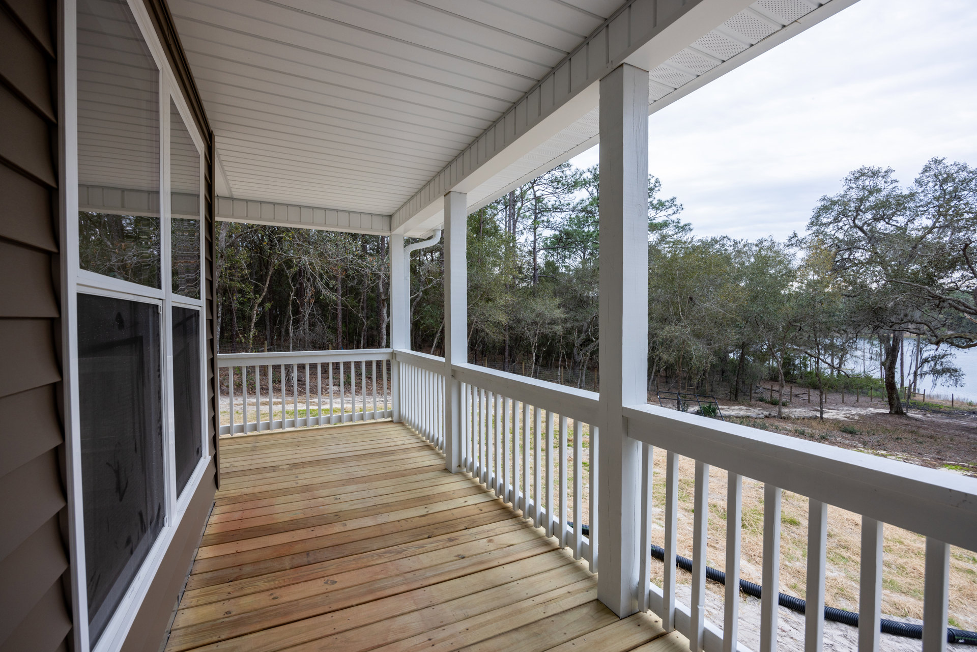 Wood deck porch with white railing, screened door, and view of trees near water