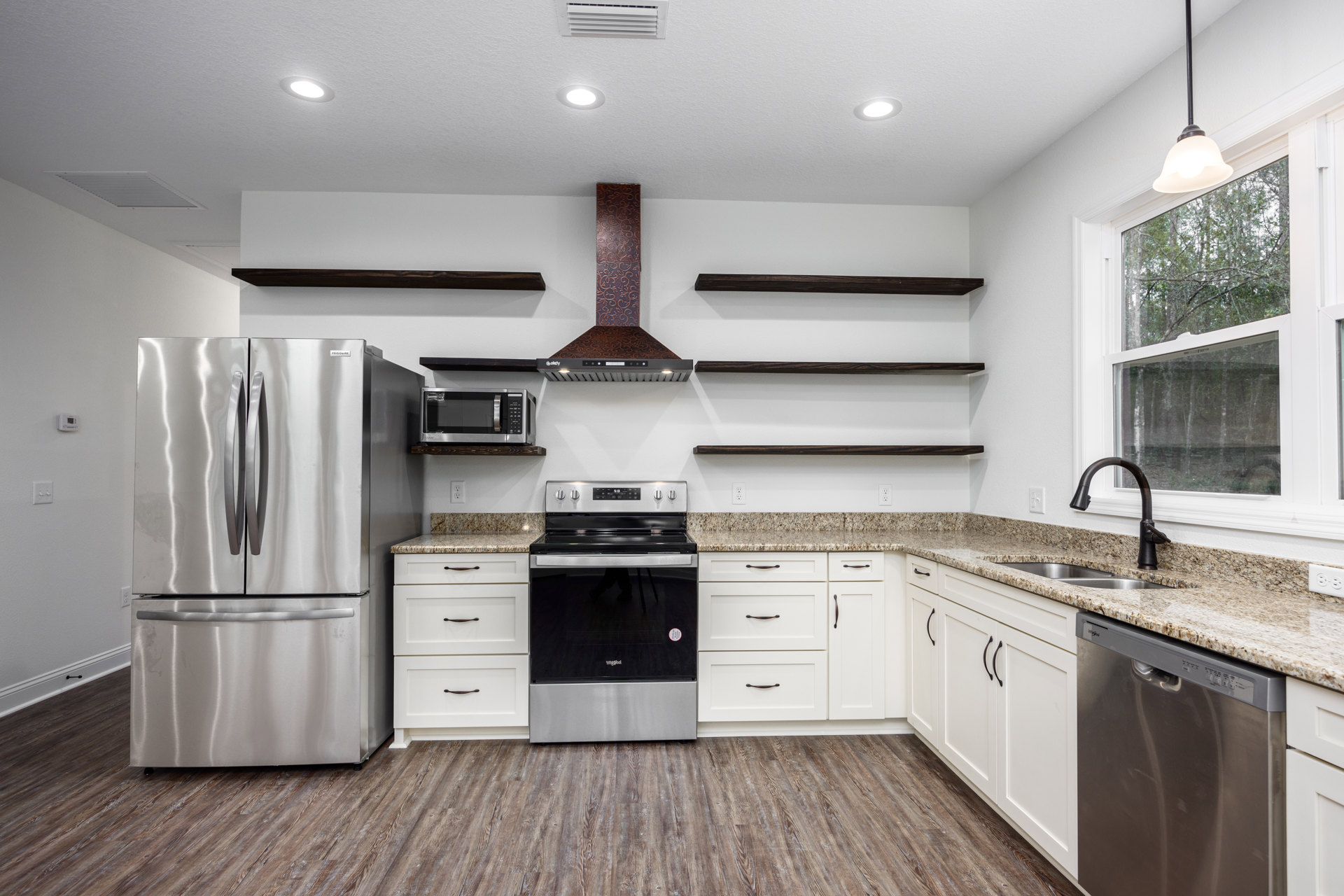 White kitchen cabinets with granite countertops, stainless steel refrigerator, black and silver stove, built-in microwave, and modern ceiling light fixture