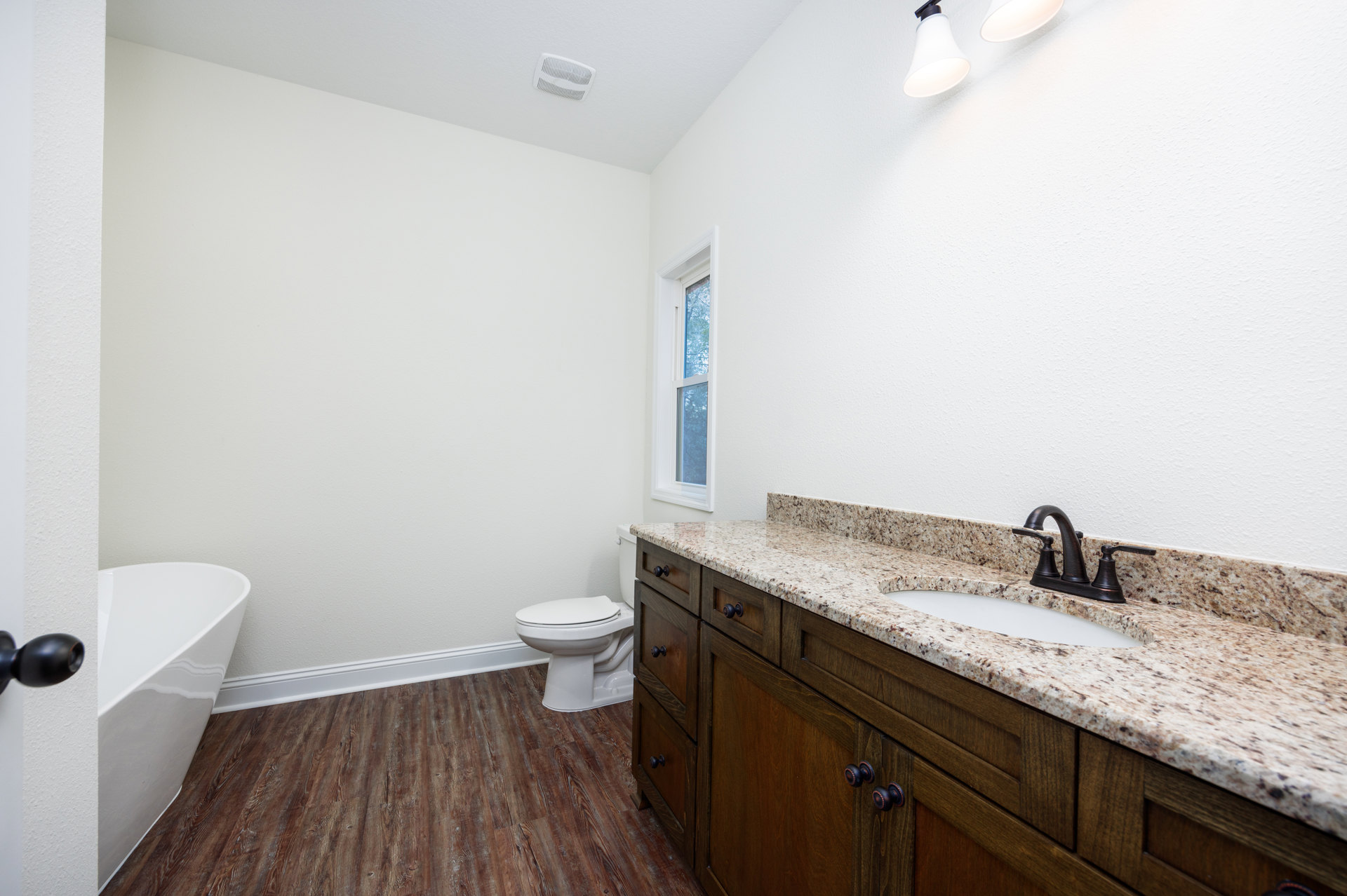 Bathroom with white bathtub, marble countertop sink and cabinet, white toilet, tiled floor, and window with white frame