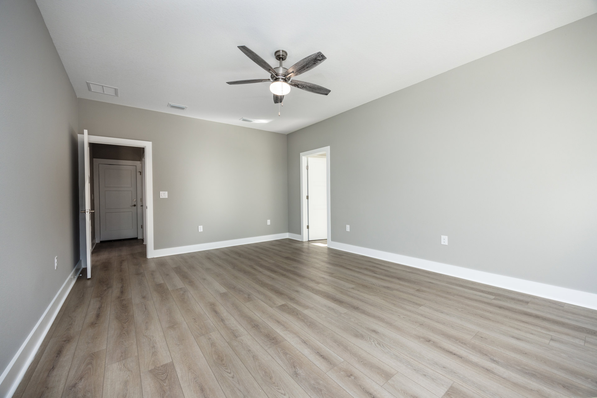Ceiling fan with light fixture mounted on white plaster ceiling above hardwood floors, open white door with silver handle and metal hinge, neutral walls, minimalist interior design