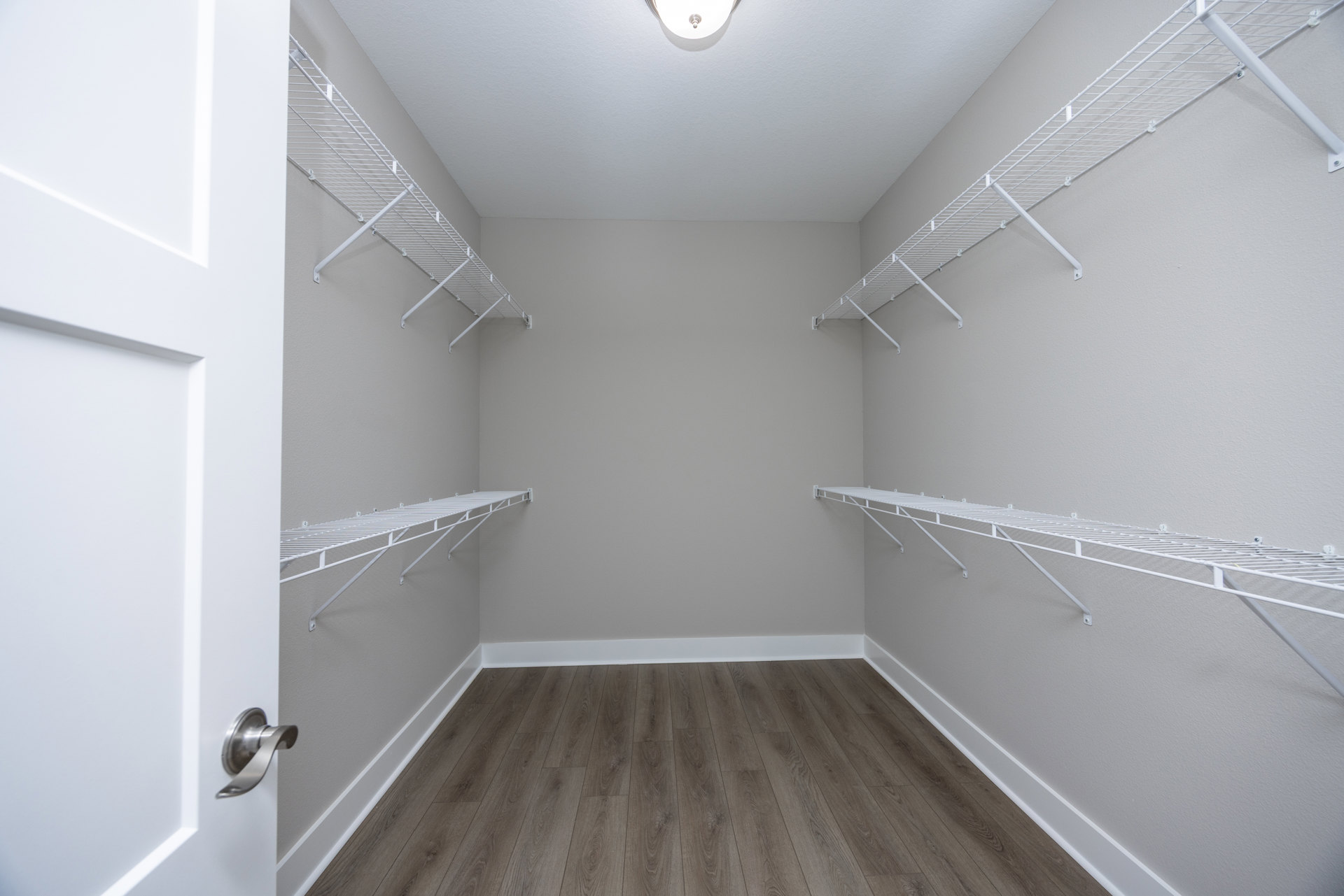 White built-in shelves against smooth white plaster walls, light wood flooring, modern ceiling light fixture, and a brushed metal door handle