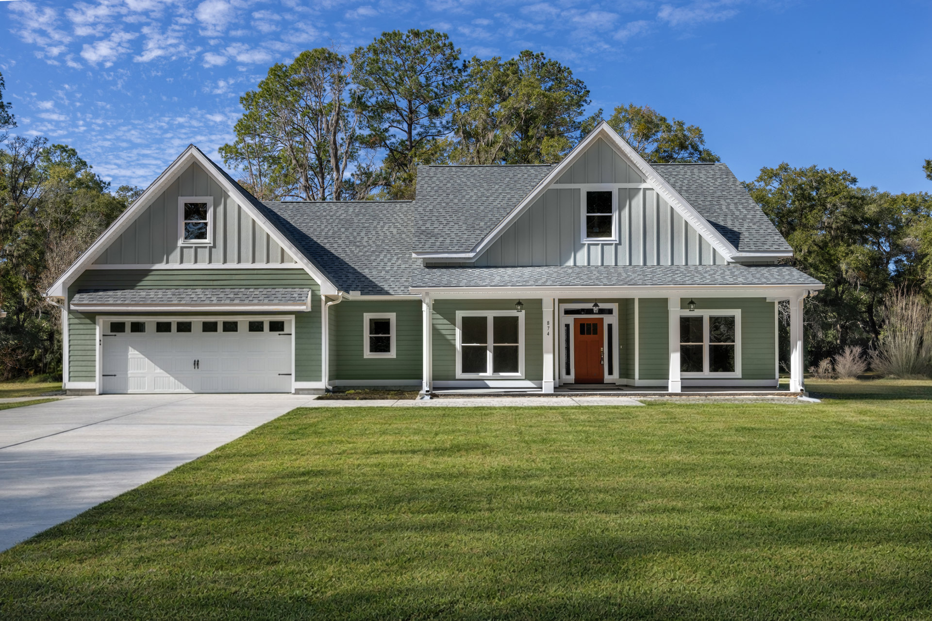 Two-story house with green siding and white trim, front porch, broken window, illuminated door, manicured lawn, paved driveway, Robert Frost Farm visible in the background.
