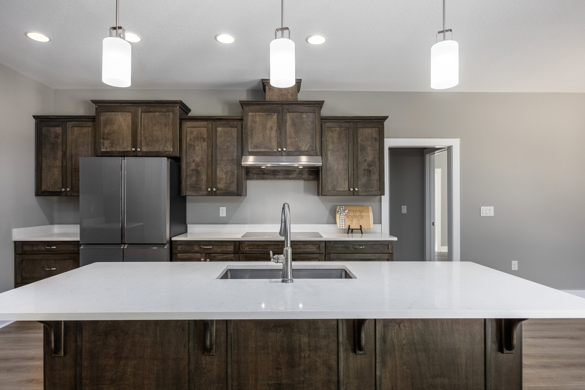 Dark wood kitchen cabinets, white countertop, stainless steel sink with modern faucet, double-door refrigerator, white metal-framed ceiling light fixture